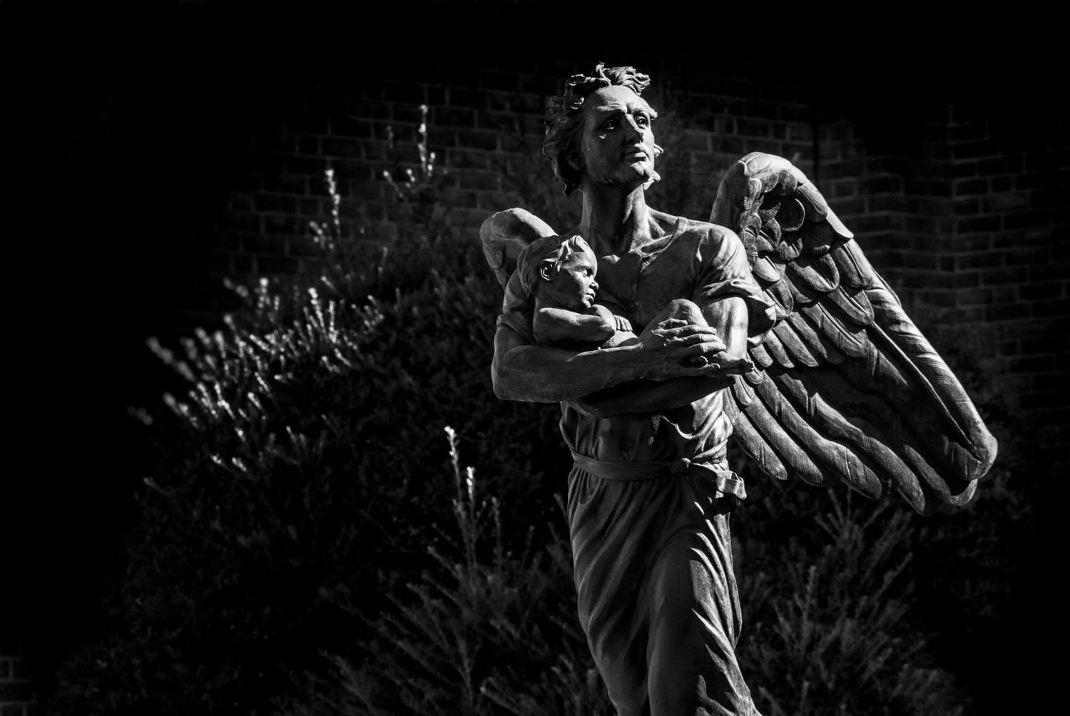 A dramatic black and white image of a Archangel Gabriel folding a  child