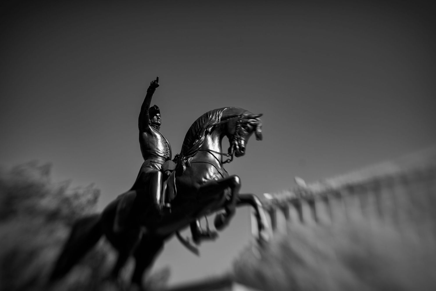 Black and white photo of a equestrian statue with motion blur effect against a clear sky.