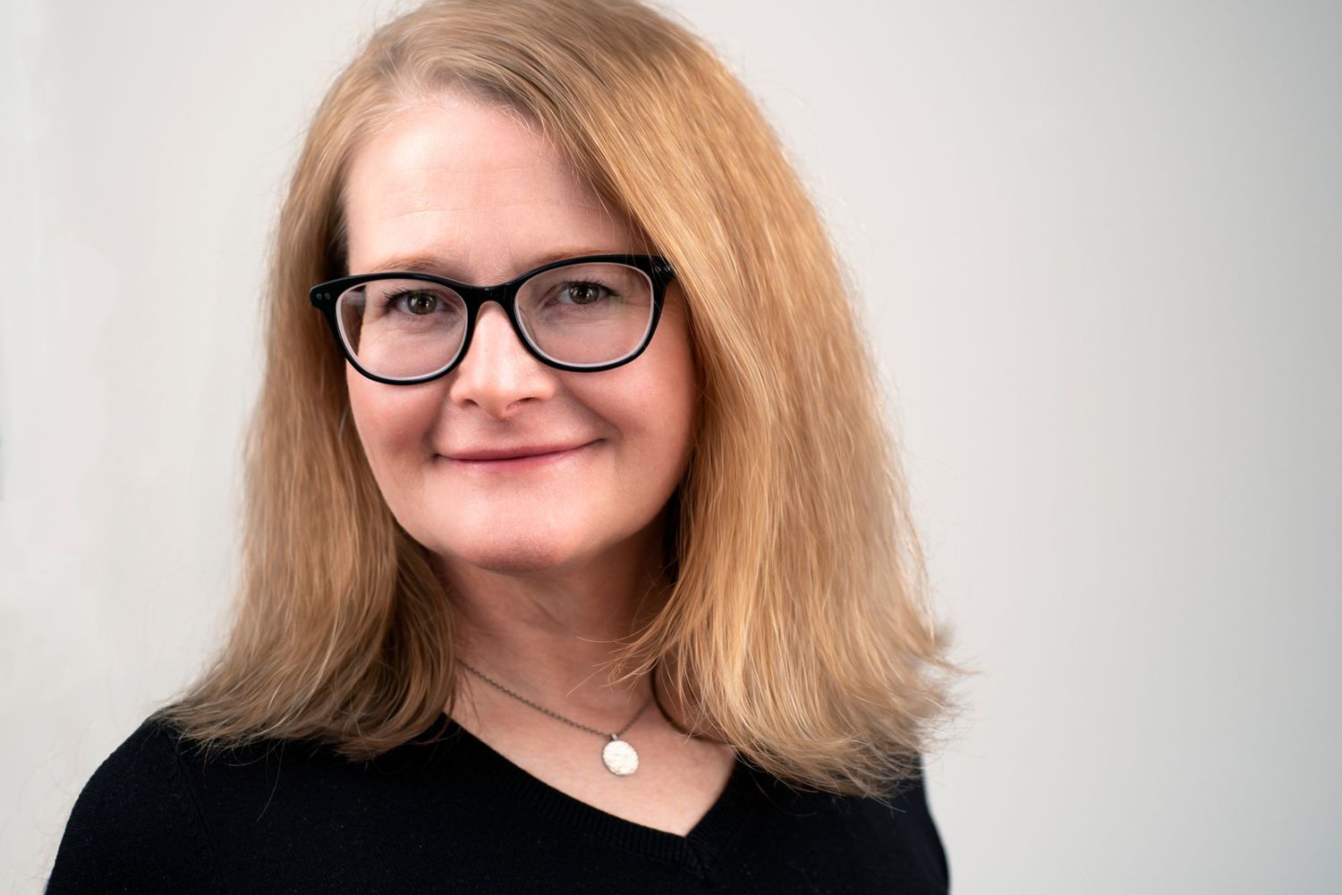Professional headshot of a pwoman wearing glasses and black top against light background.