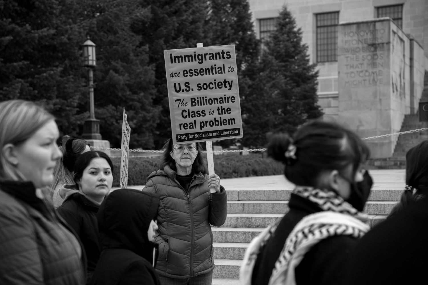 Black and white photo of protesters holding signs about immigration at a public gathering.
