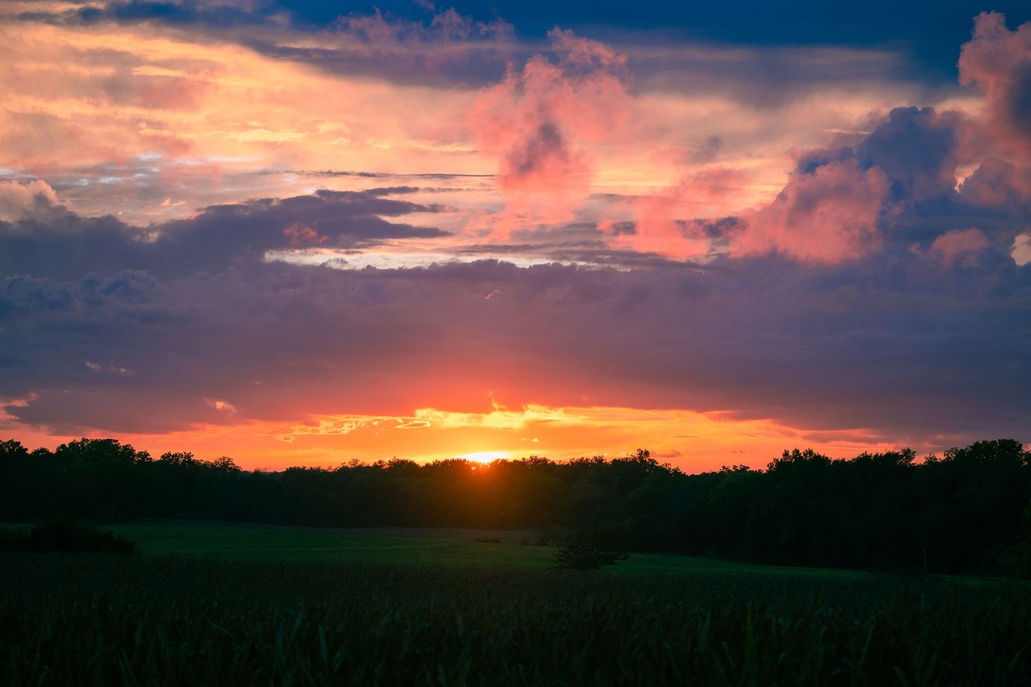 Dramatic sunset panorama with vibrant orange clouds over silhouetted landscape.