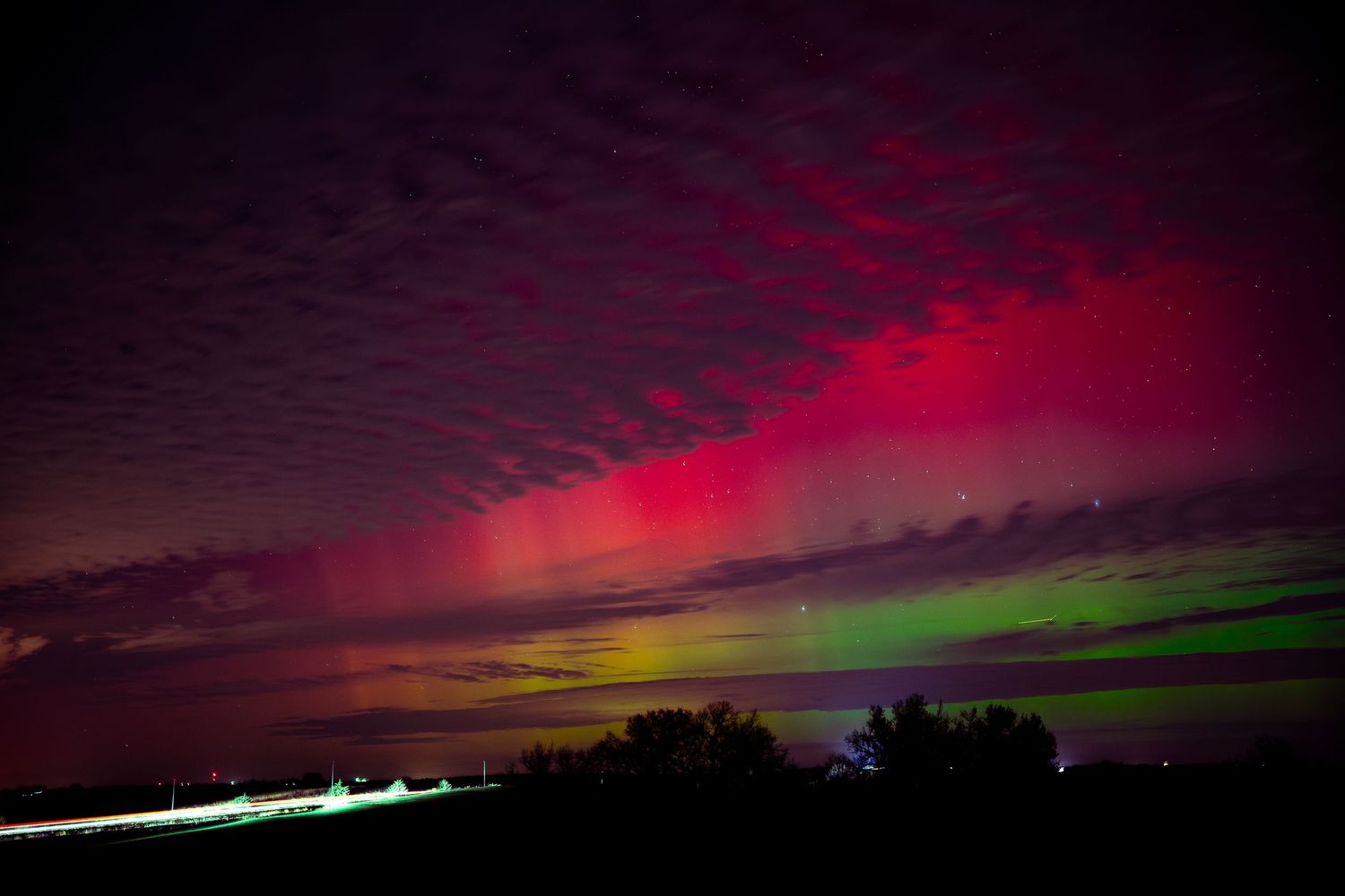 Vibrant red and green aurora borealis lights dancing across the dark night sky.