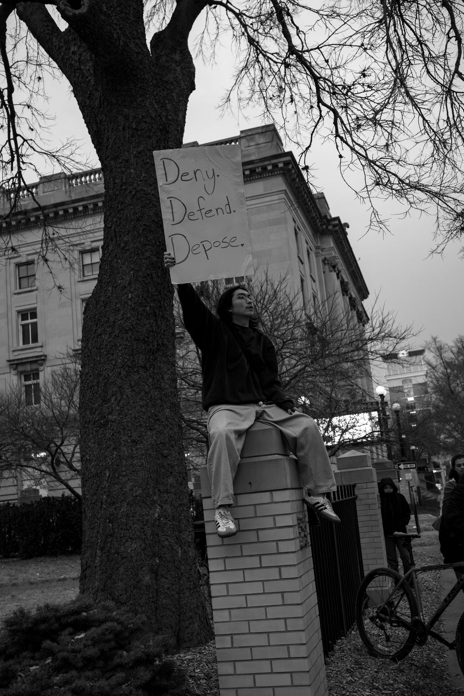Black and white image of protesters with signs standing near brick walls and trees.