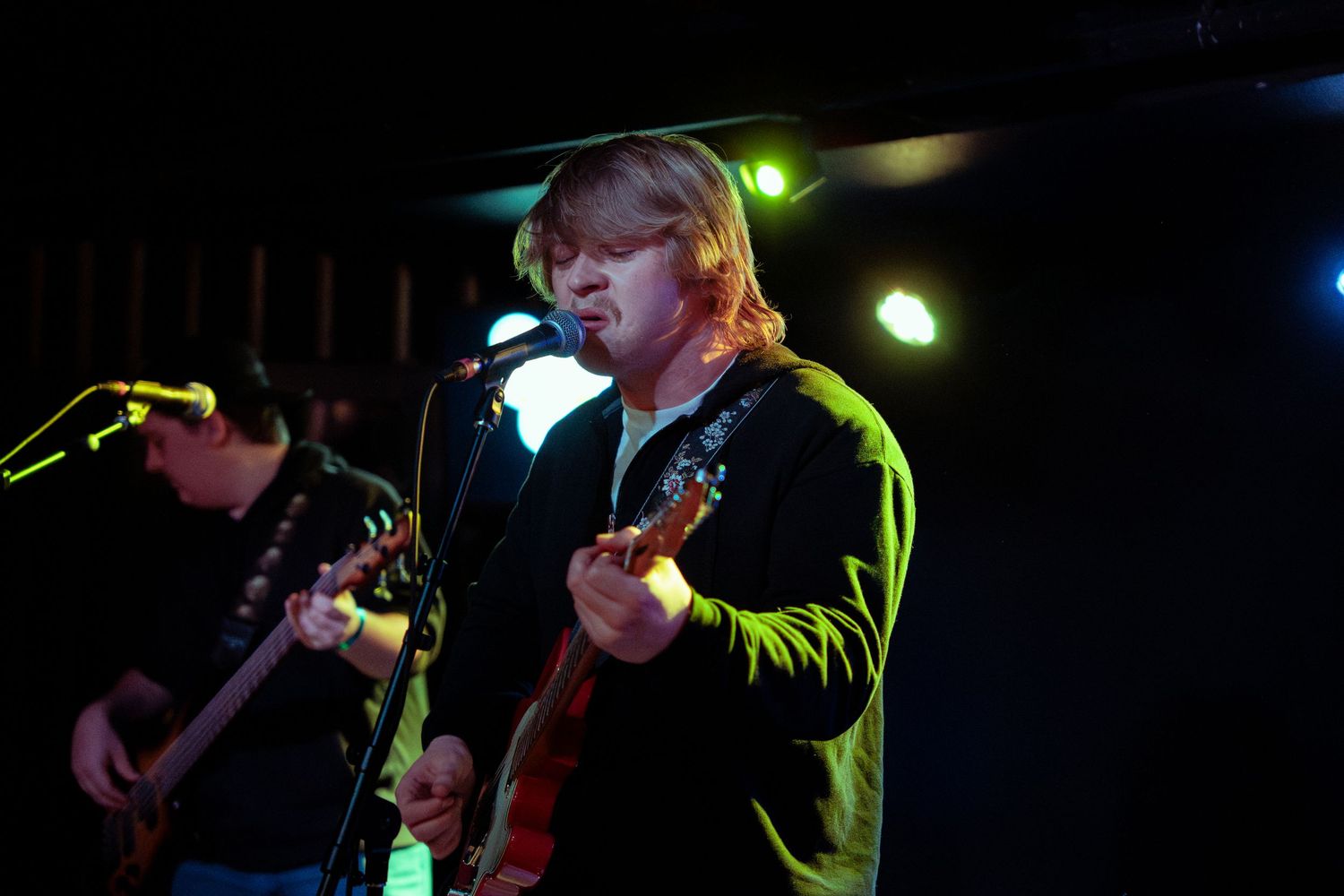 Musicians perform on stage under dramatic green and blue lighting during a live concert performance.