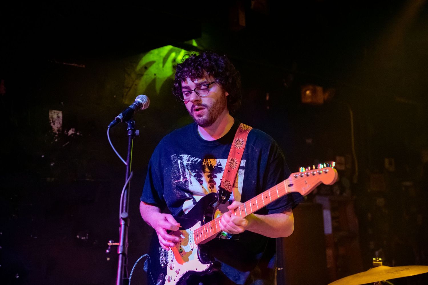 A musician performs on stage with an electric guitar under colorful lighting at a live concert venue.