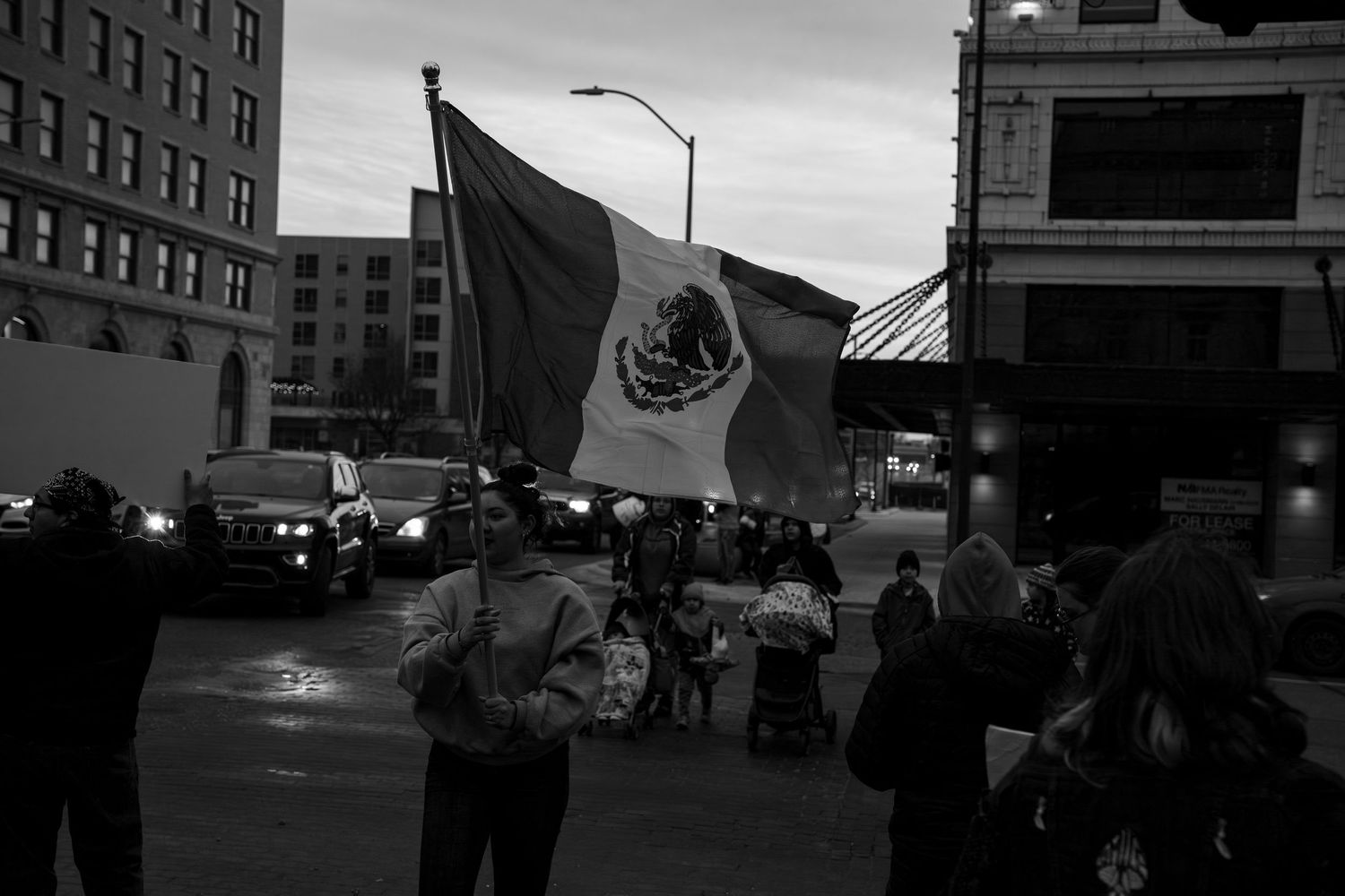 Silhouettes of protesters marching with signs against an urban skyline at dusk.