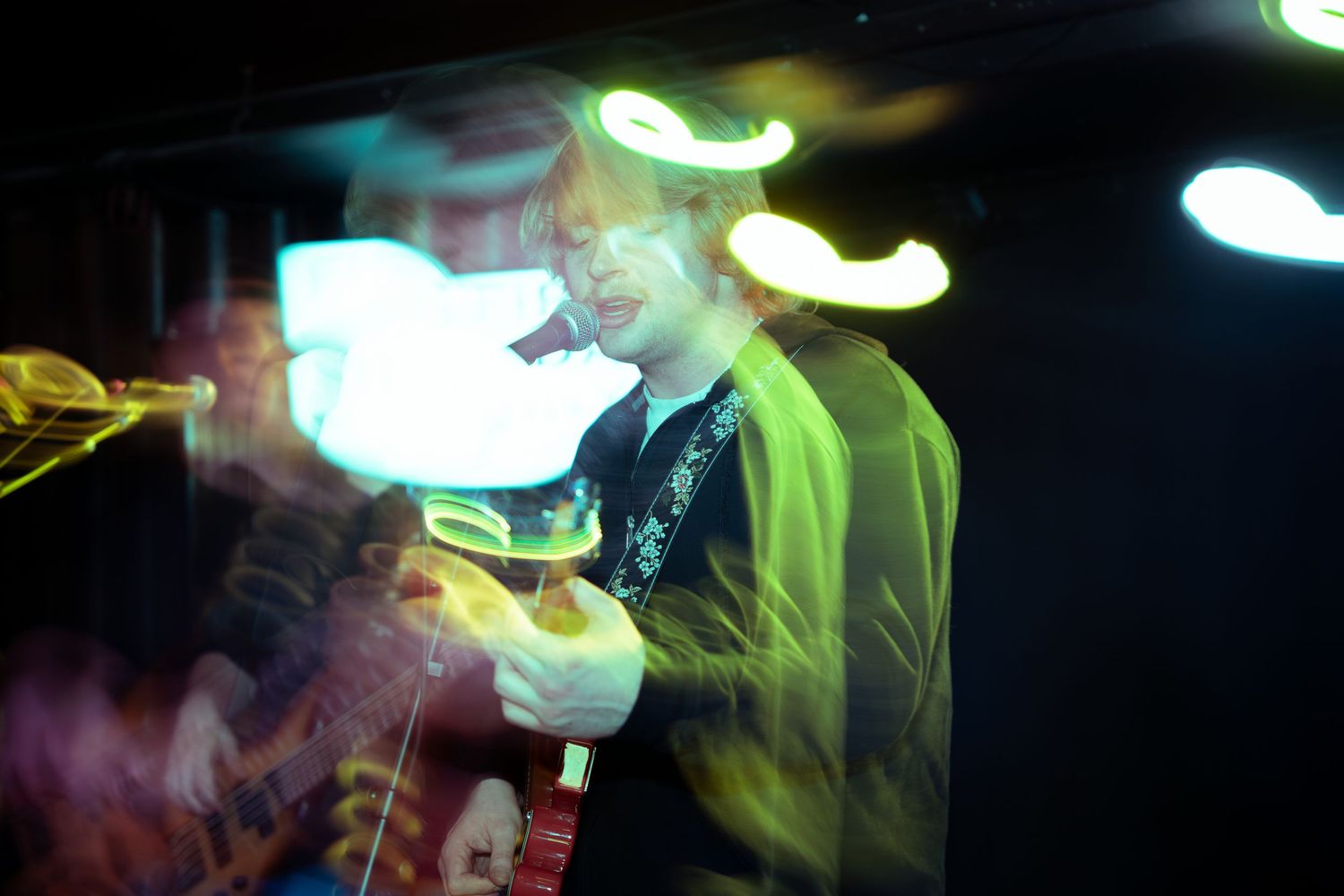 Guitarist performs energetically on stage under colorful spotlights with motion blur effects.