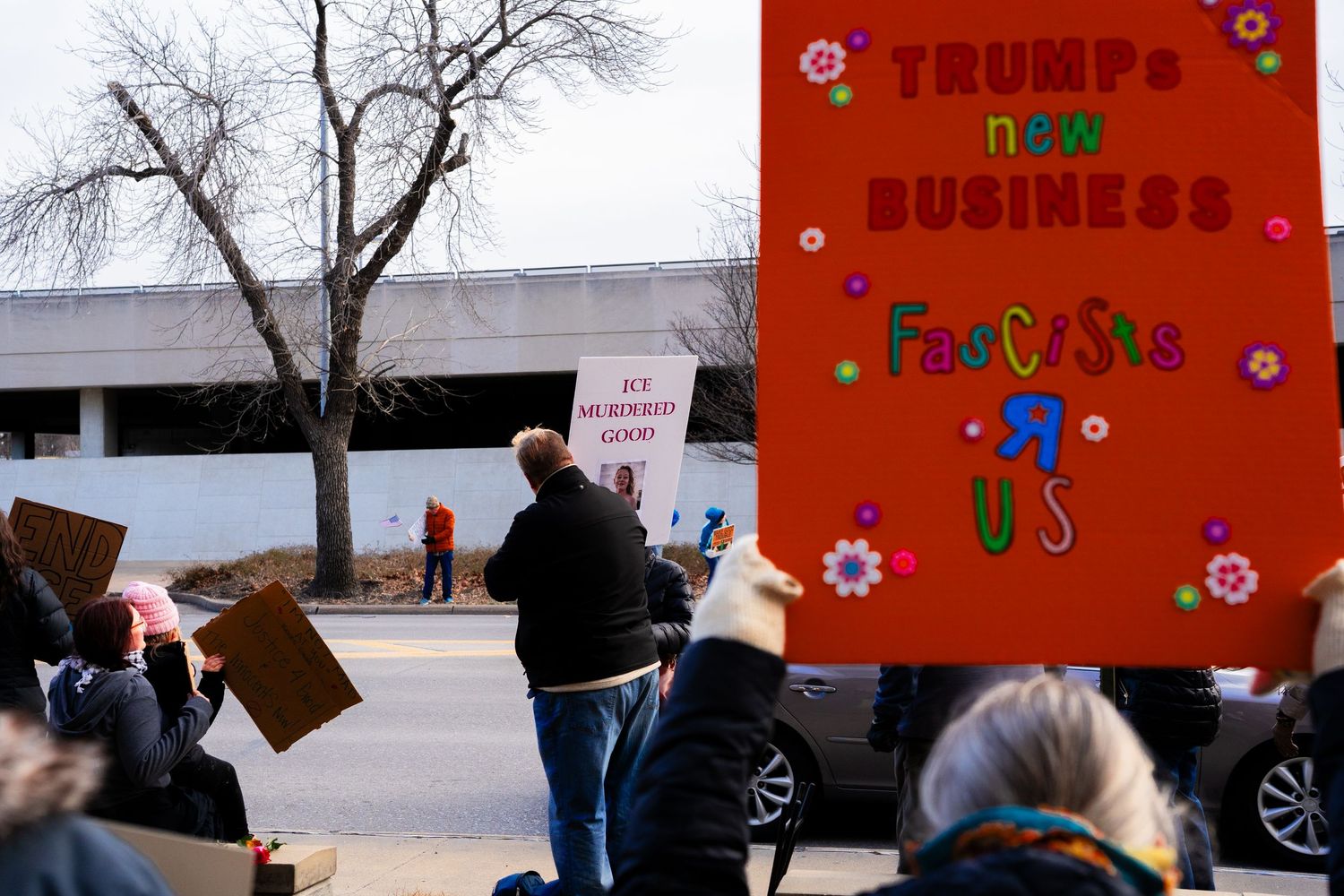 Red protest sign with colorful decorations amid crowd of demonstrators.