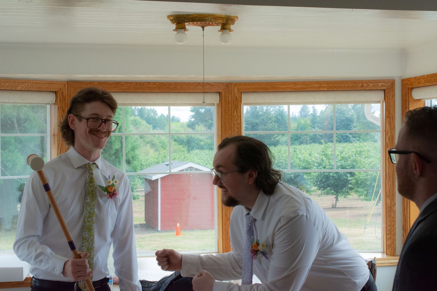 People gathered in a bright room with large windows and wooden trim during a social event.