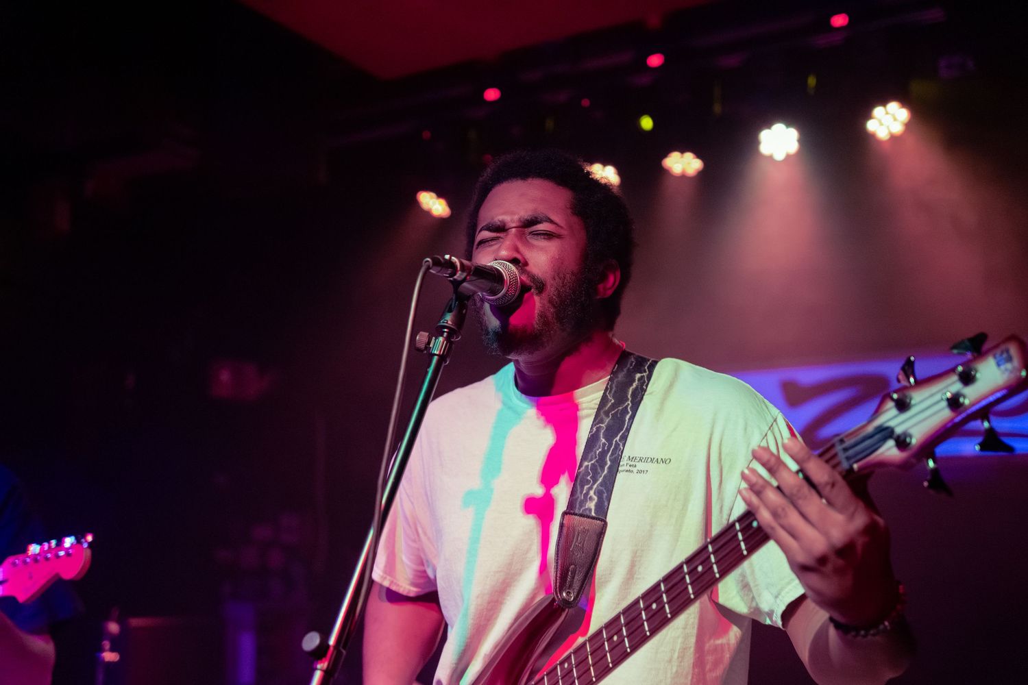 Musicians perform on stage under colorful purple and pink lighting during a live concert performance.