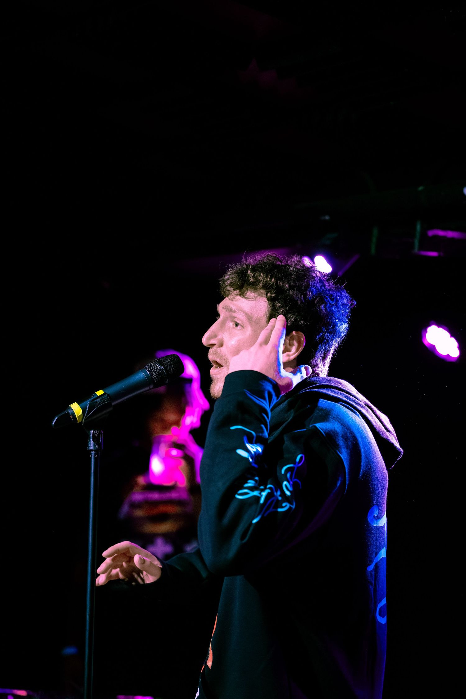 Singer performing passionately with hand to ear under purple and blue stage lighting.