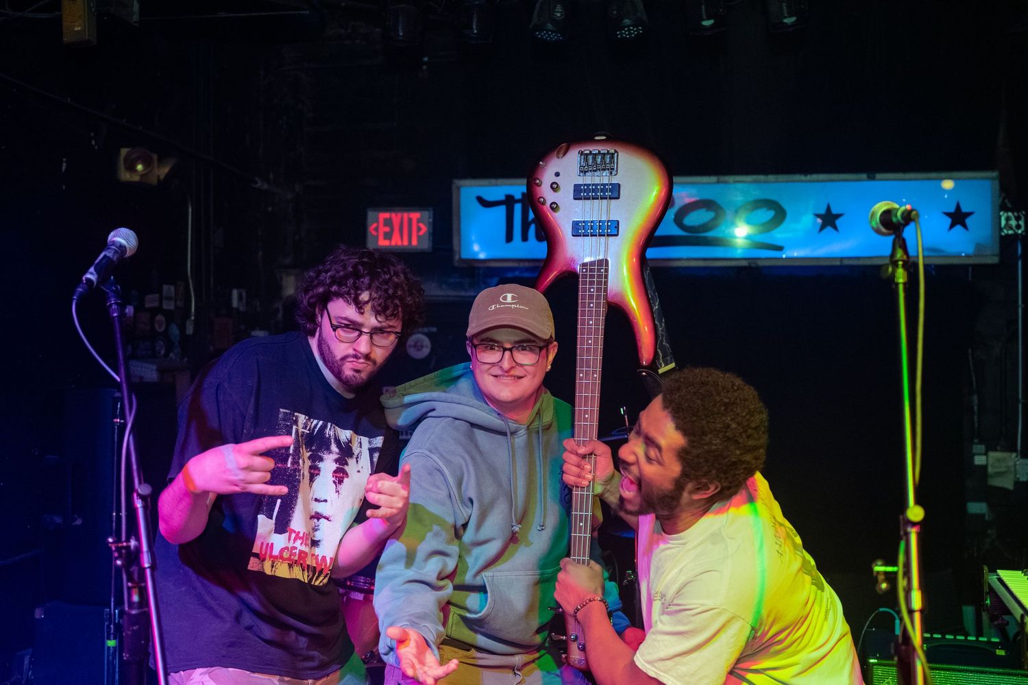 Musicians performing on stage under colorful pink and blue lighting at a nightclub venue.