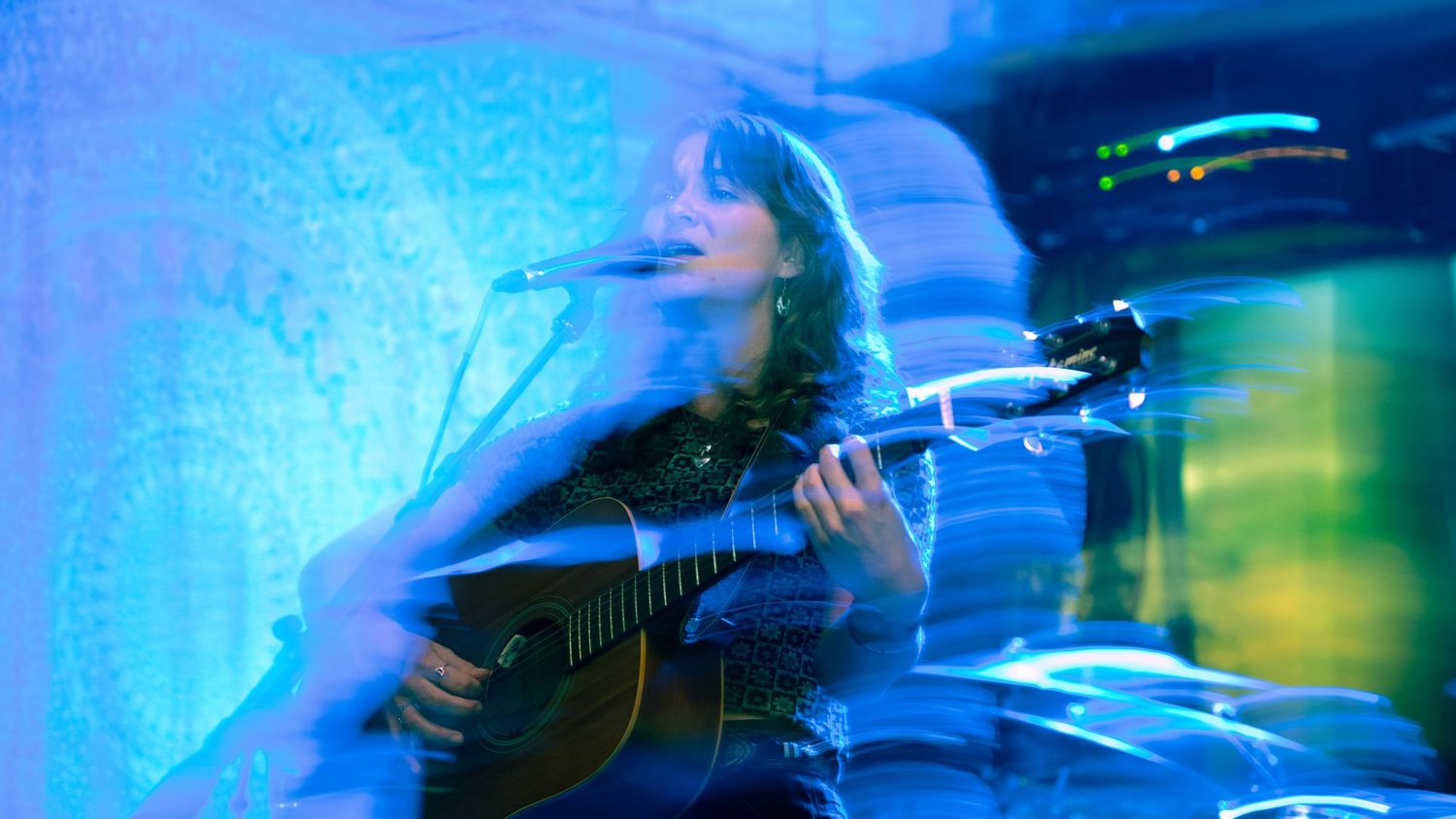 Abstract blue-tinted concert photography showing musician with guitar in motion blur.