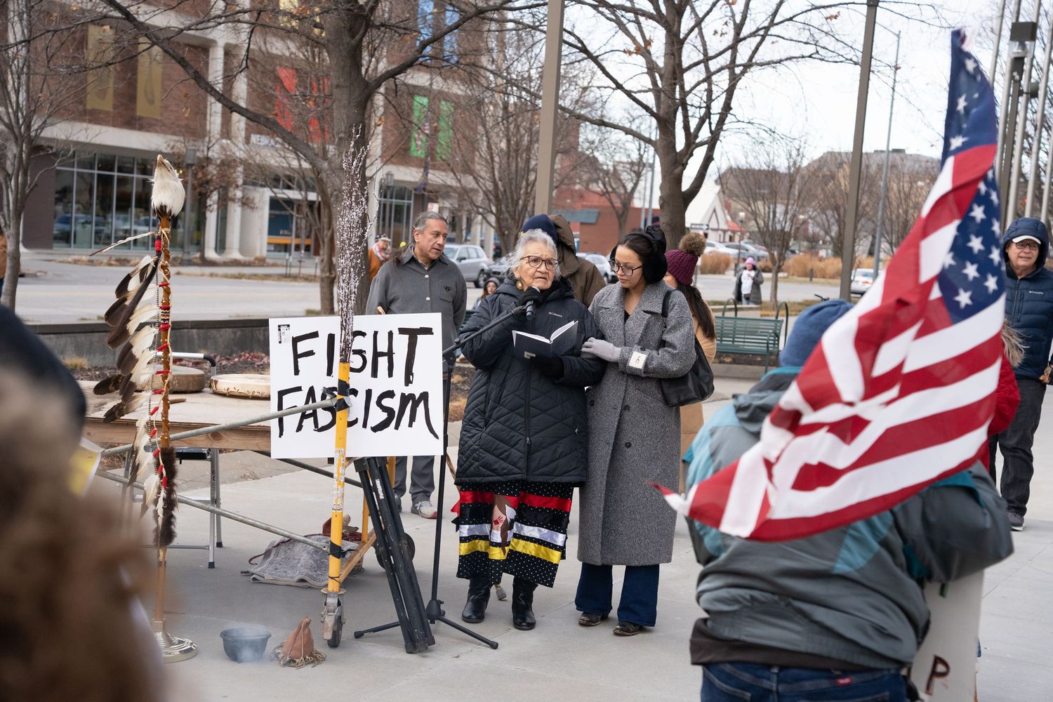 Protesters hold signs and American flags at an outdoor demonstration against fascism.
