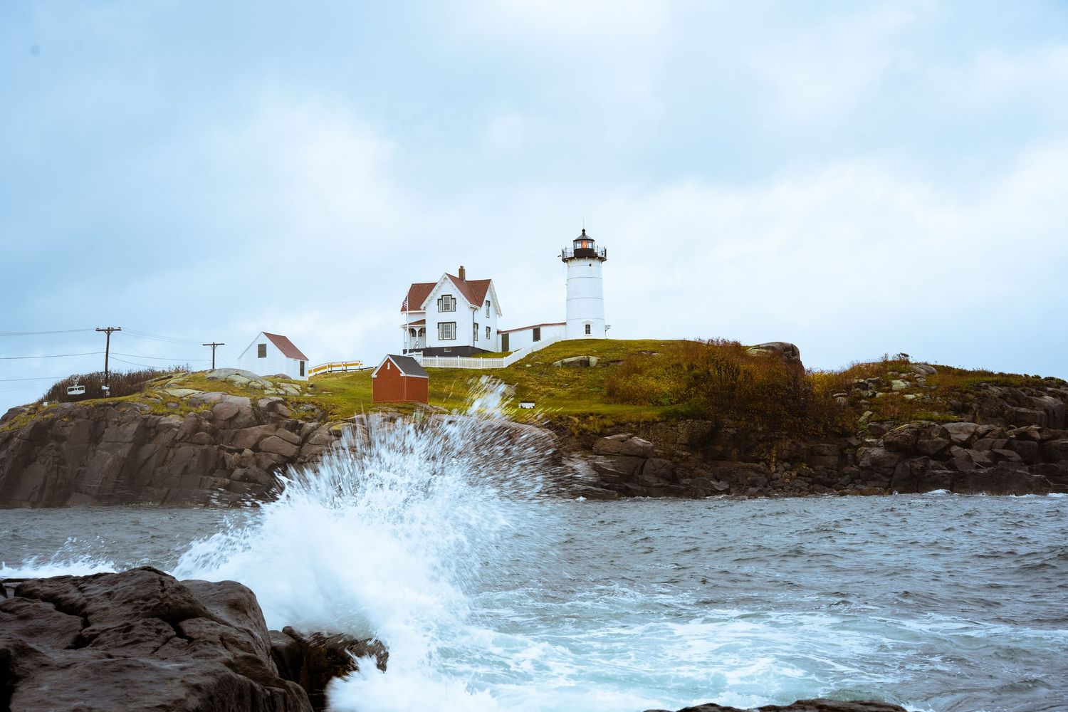 Dramatic waves splash against a rocky shore near a coastal lighthouse station.