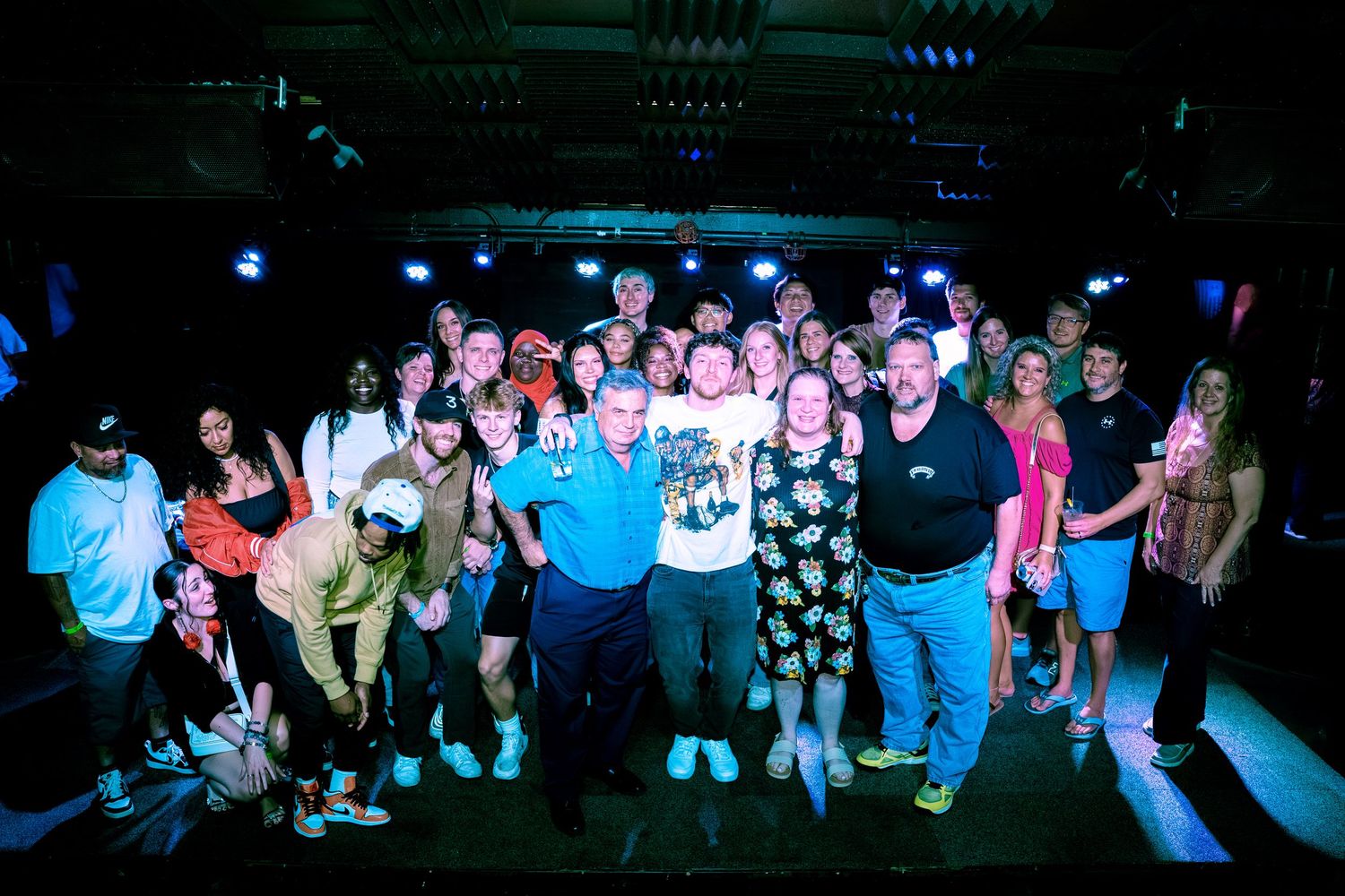 Large group photo of concert crowd under blue and pink venue lighting.