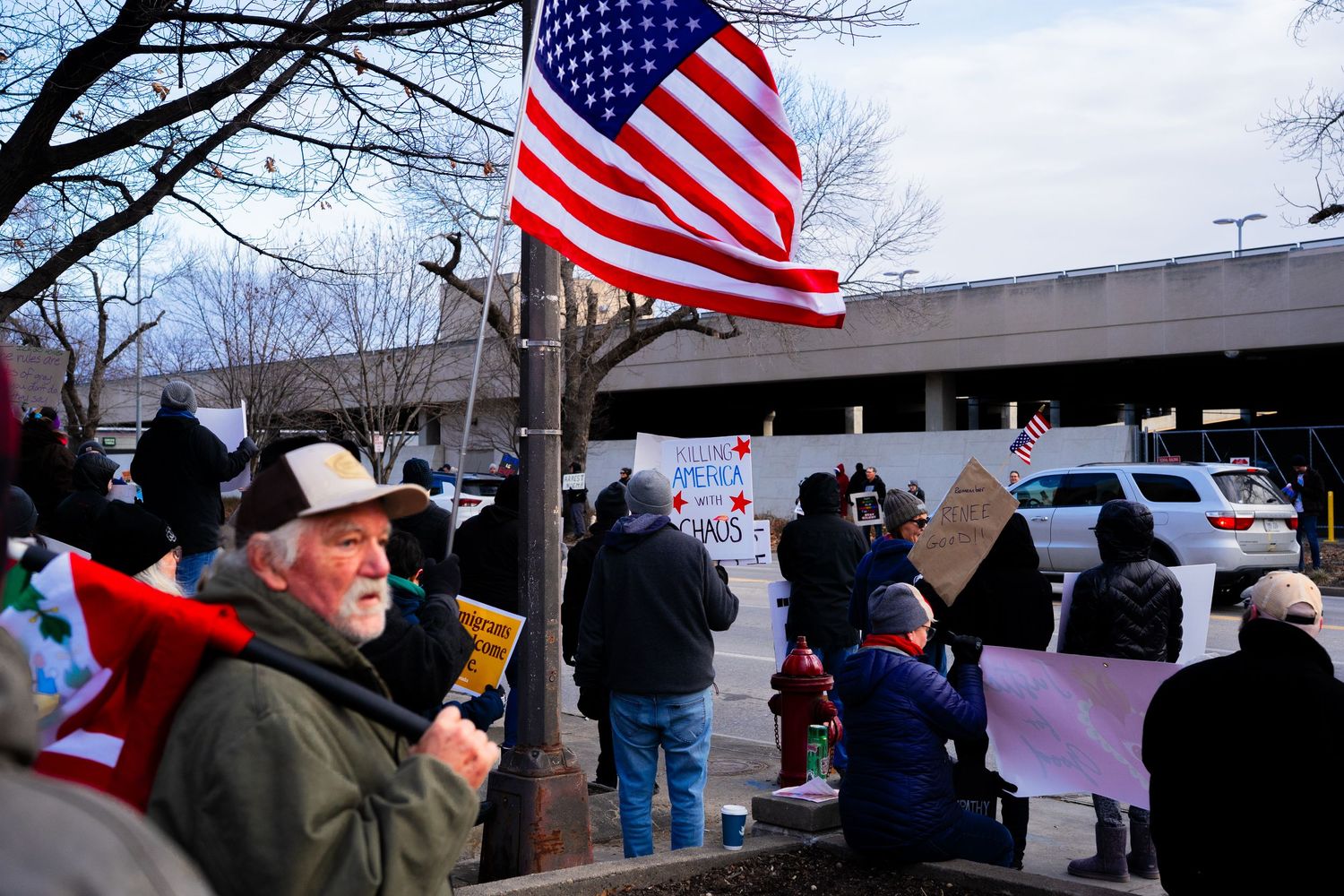 American flag waves as protesters gather for demonstration on winter day.