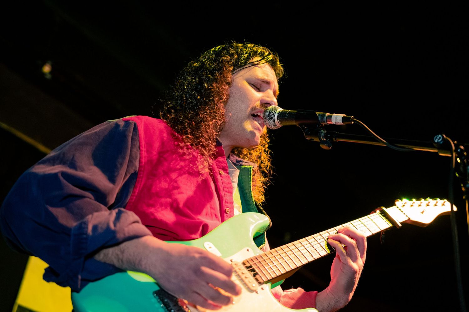 Musician performs passionately on stage with guitar under dramatic lighting during live concert performance.