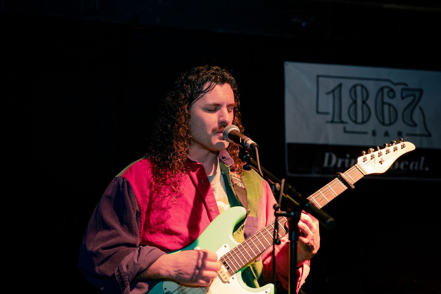 A musician performs on stage with a guitar under dramatic lighting during a live concert performance.