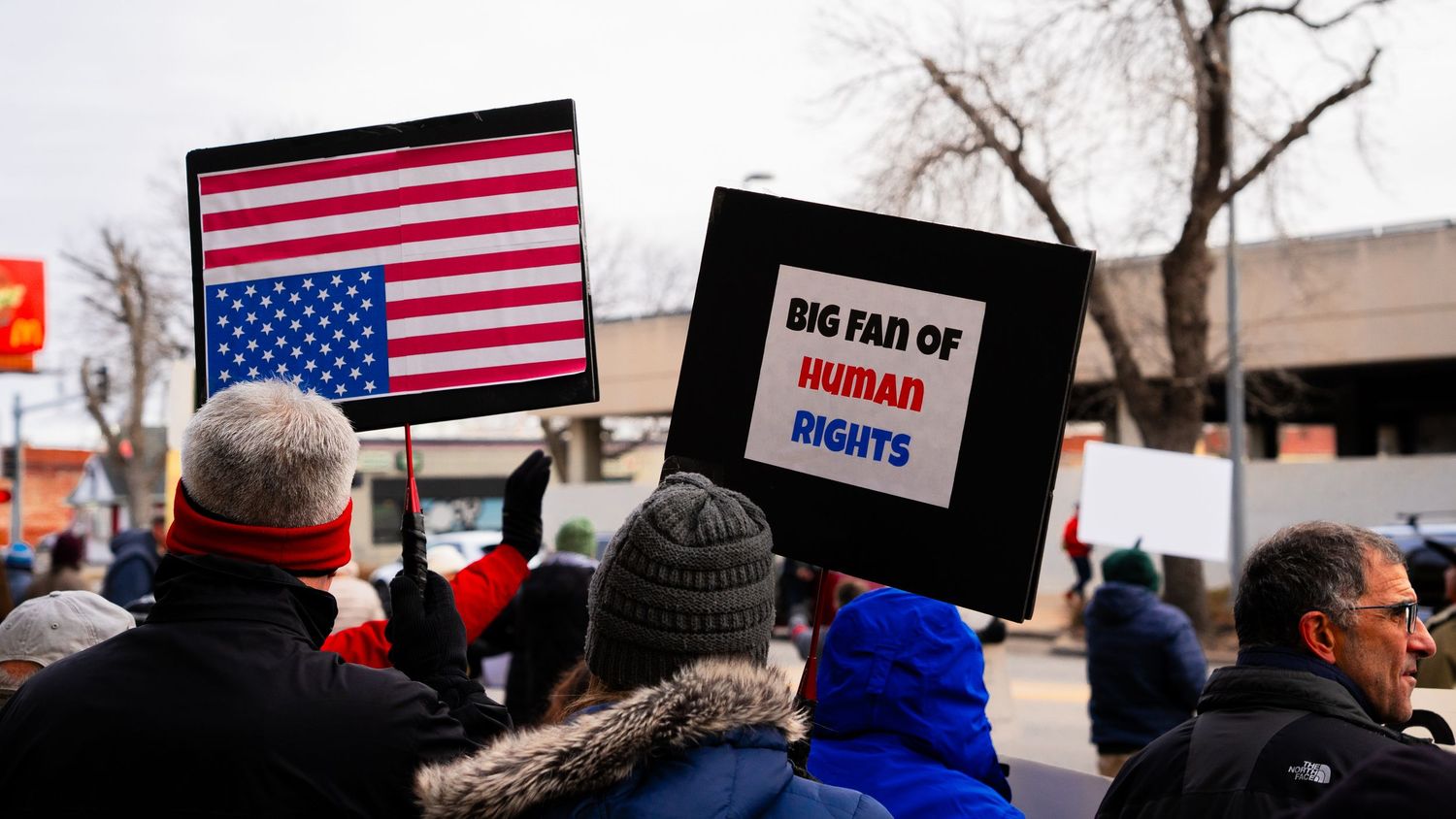 Protesters hold American flags and signs during a political demonstration in winter.