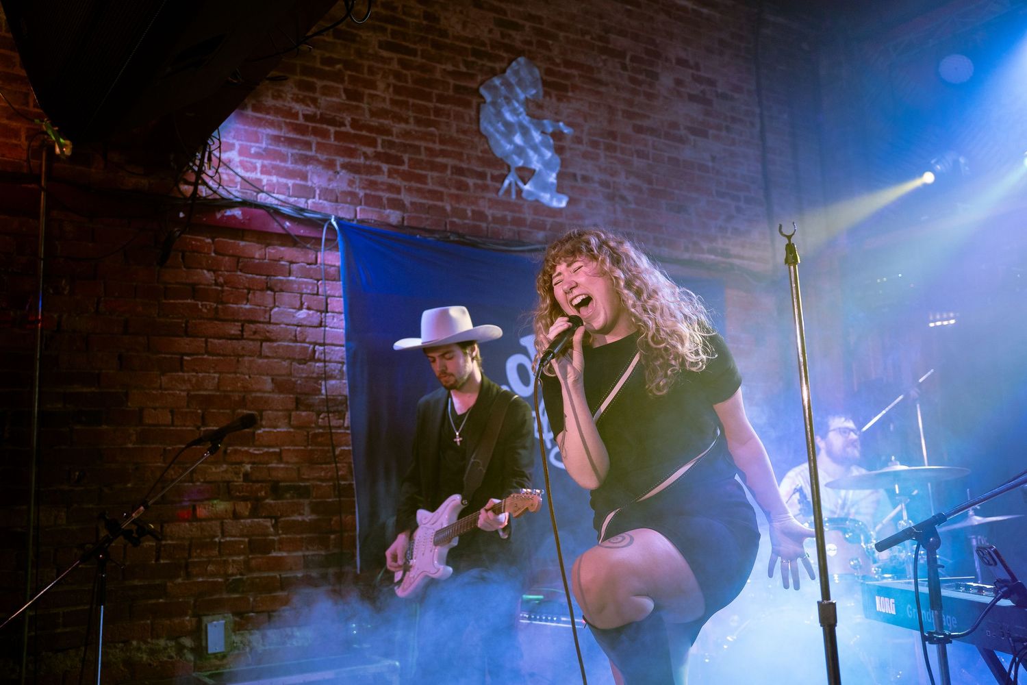 Concert performance with blue stage lighting and atmospheric fog effects.