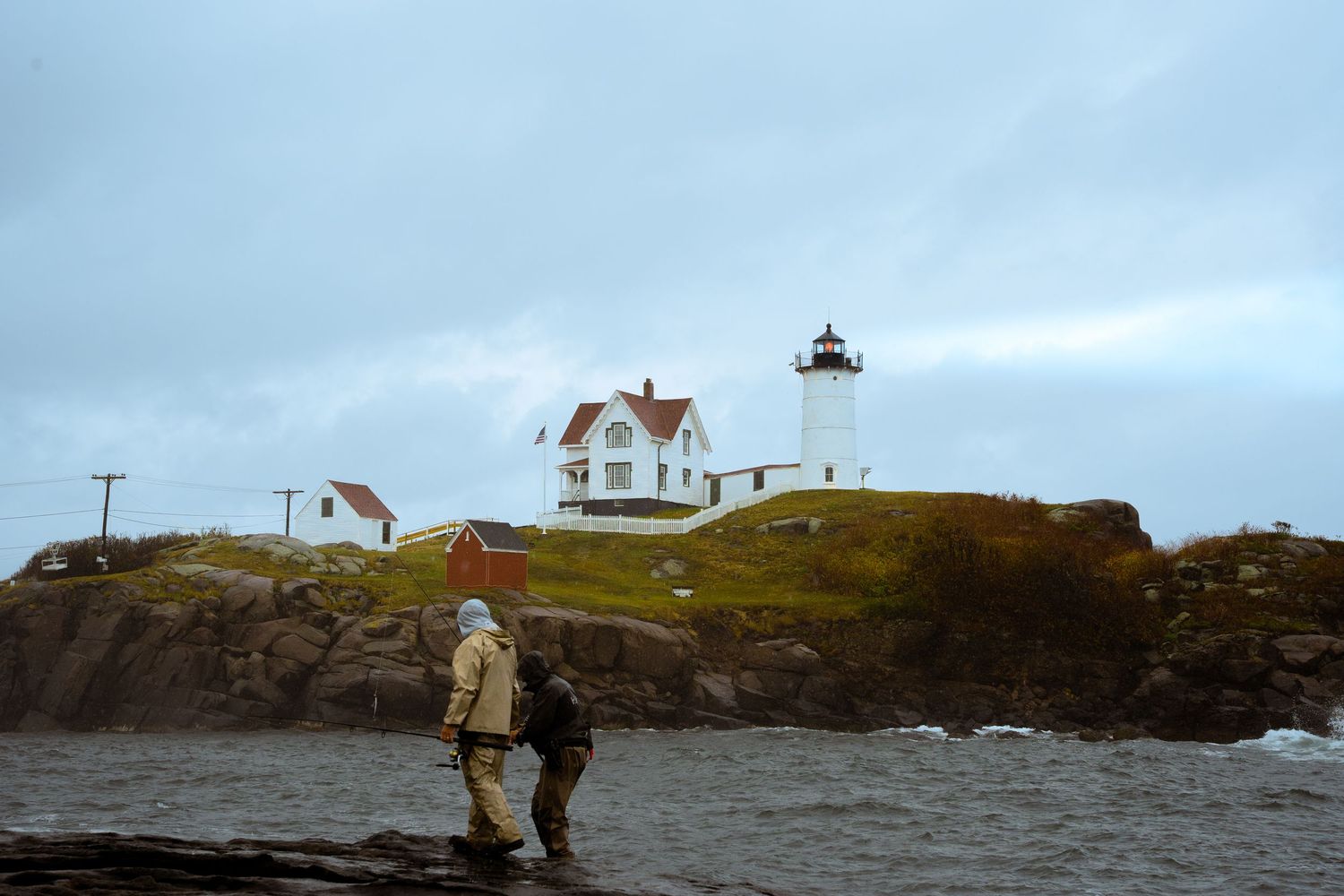 A lighthouse perches on rocky coastal cliffs under an overcast sky.