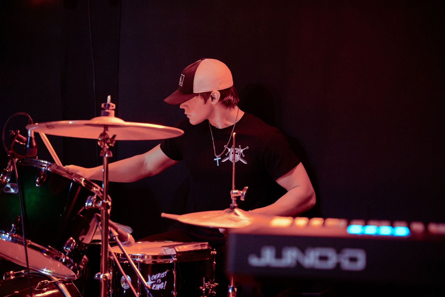 Close-up shots of drum cymbals and musical equipment illuminated in pink and blue stage lighting during a performance.