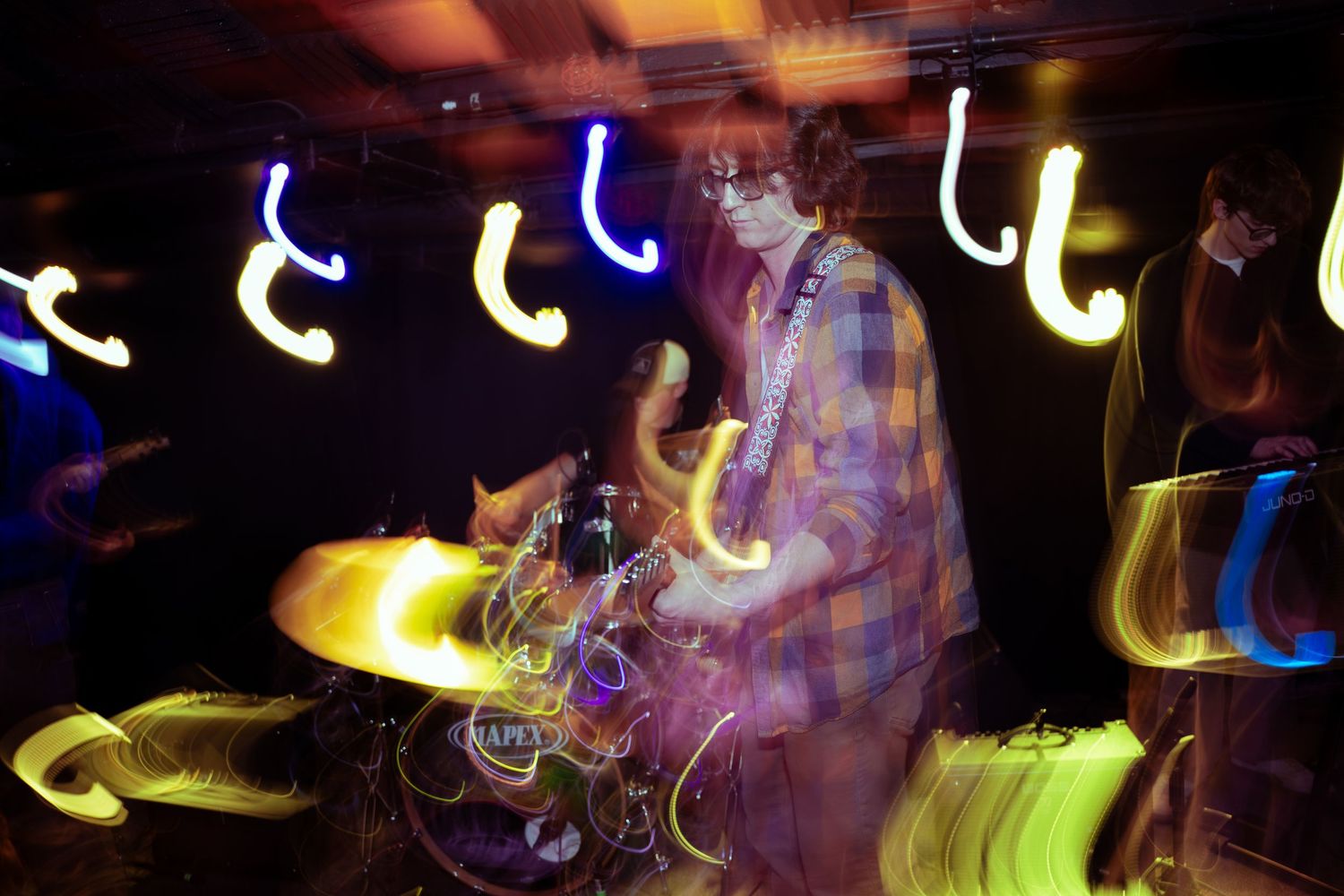 Long exposure photograph showing colorful light trails creating abstract patterns against a dark background.
