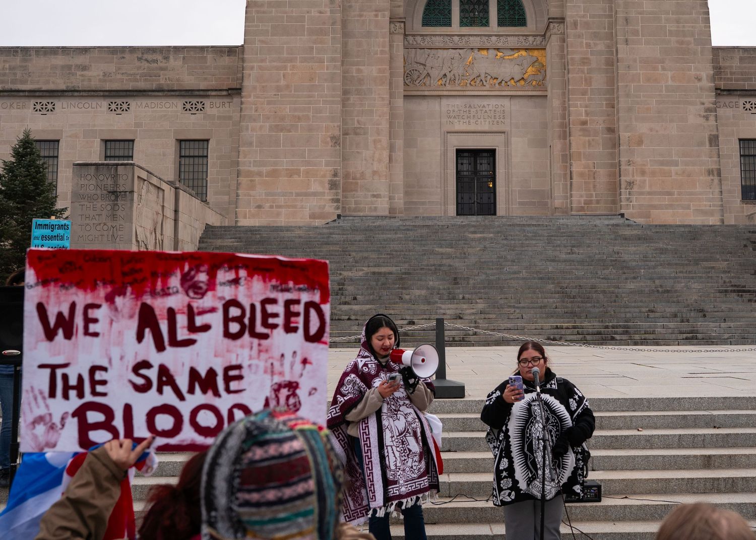 Protesters with handmade signs gather on stone steps of a government building.