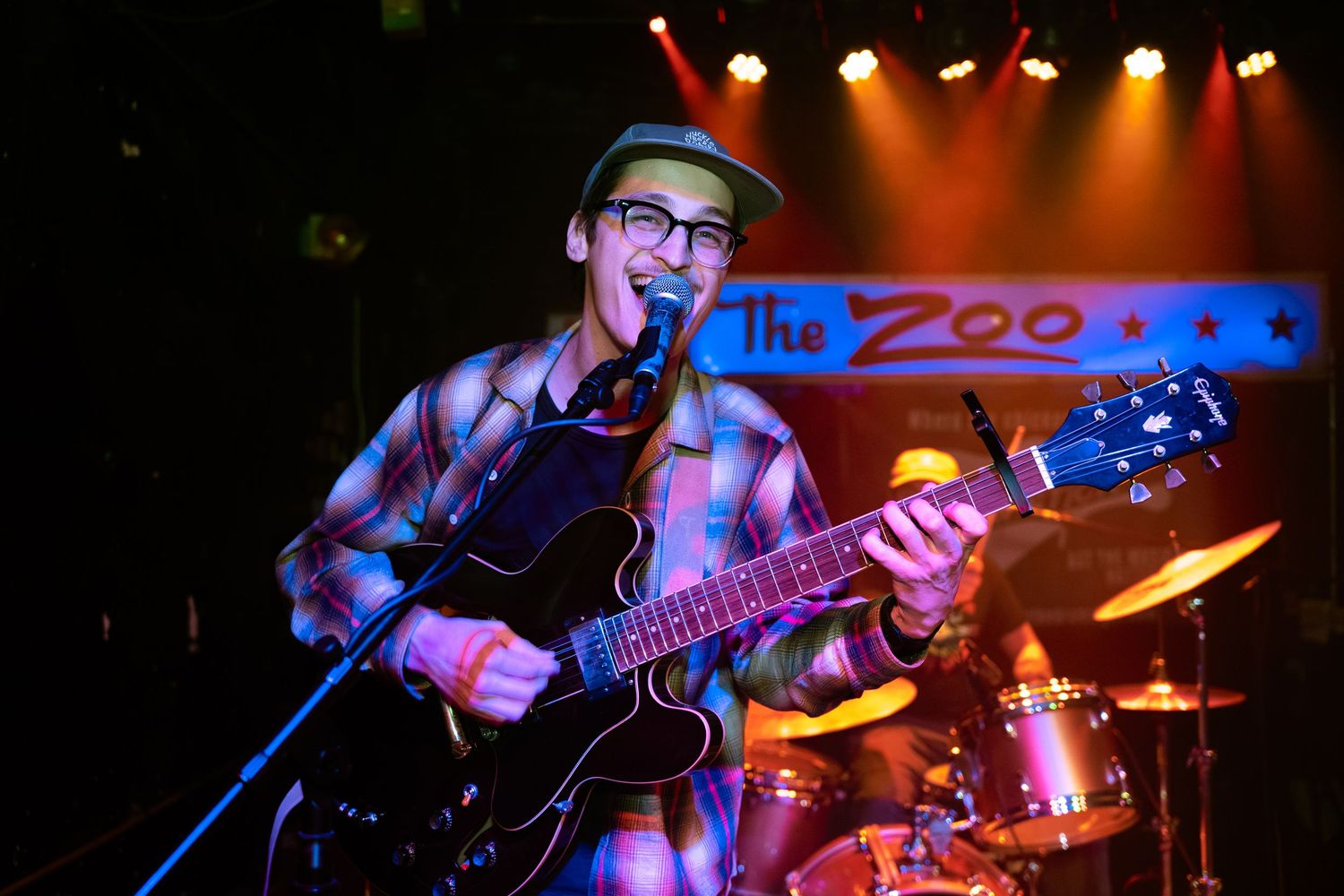 A musician performs on stage with a guitar under colorful blue and red stage lighting at a live music venue.