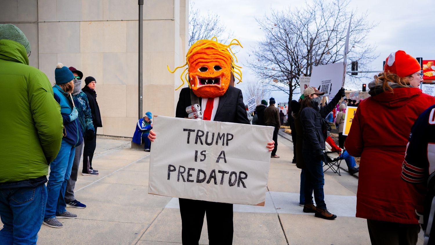 Protesters gather outside a building with signs and colorful winter clothing.