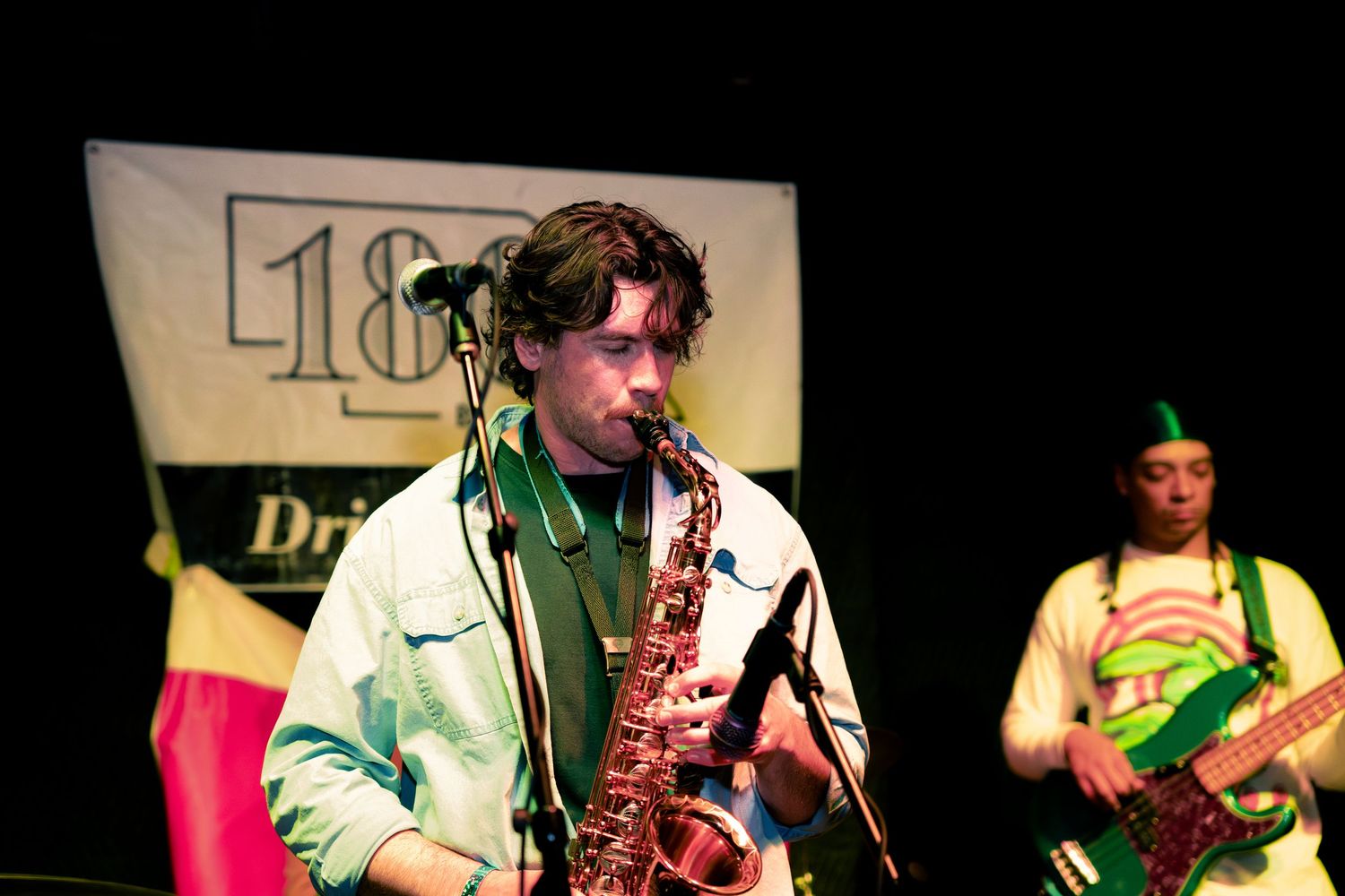 Musicians perform on stage with guitars and saxophone during a live concert performance.