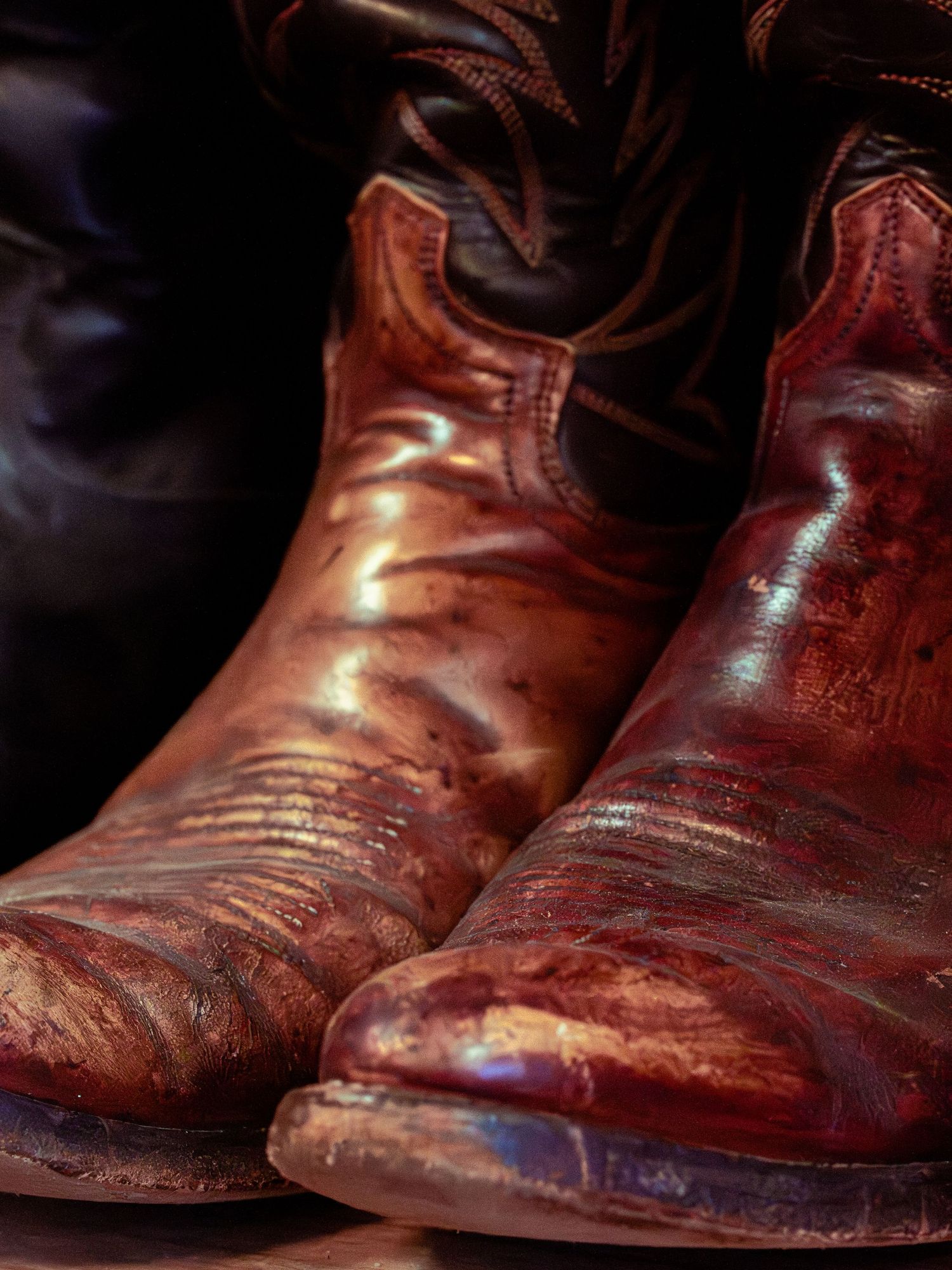Weathered brown leather cowboy boots showing patina and wear against dark background.