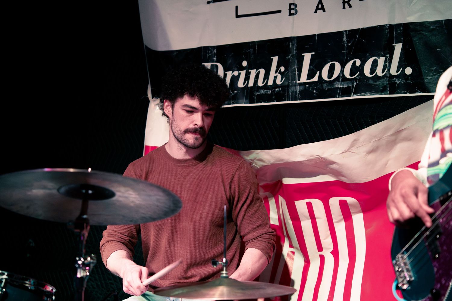 A person in a red shirt sits at a bar counter with striped decor and signage visible in the background.