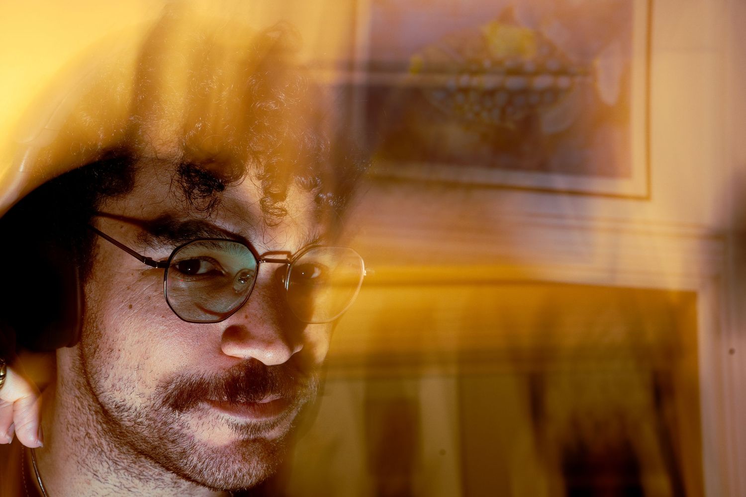 Warm golden-tinted portrait showing someone with glasses in contemplative side view.