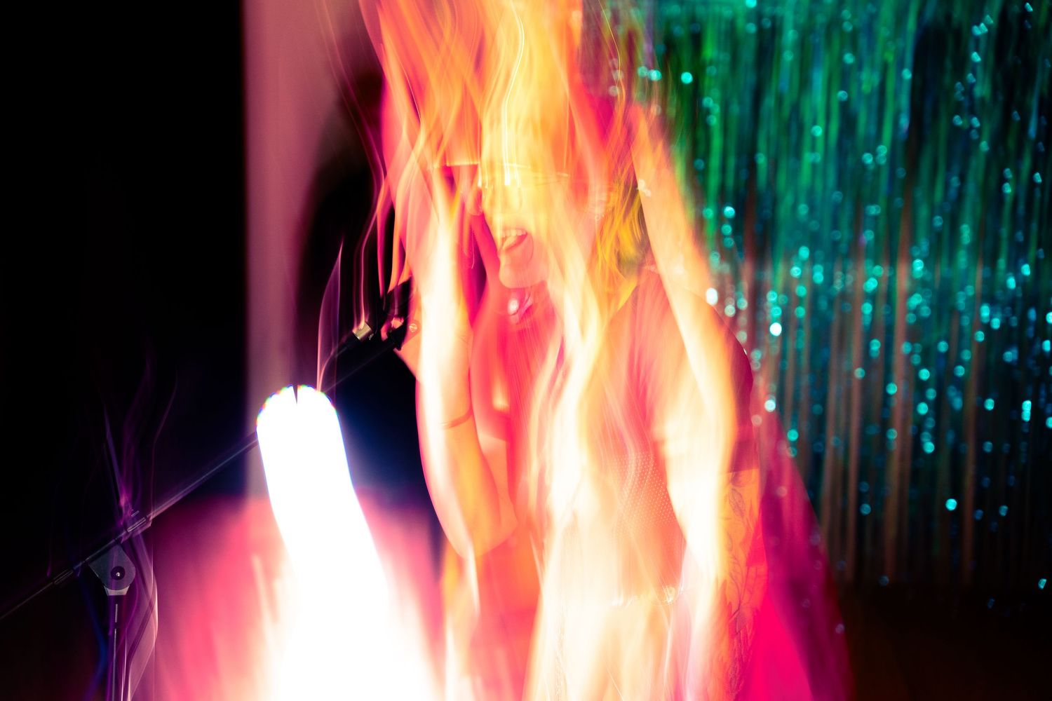 Colorful flame-like light effects against dark background with teal sparkles.