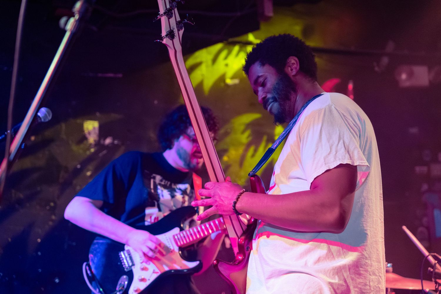 Musicians perform on stage with colorful purple and yellow lighting effects during a live concert performance.