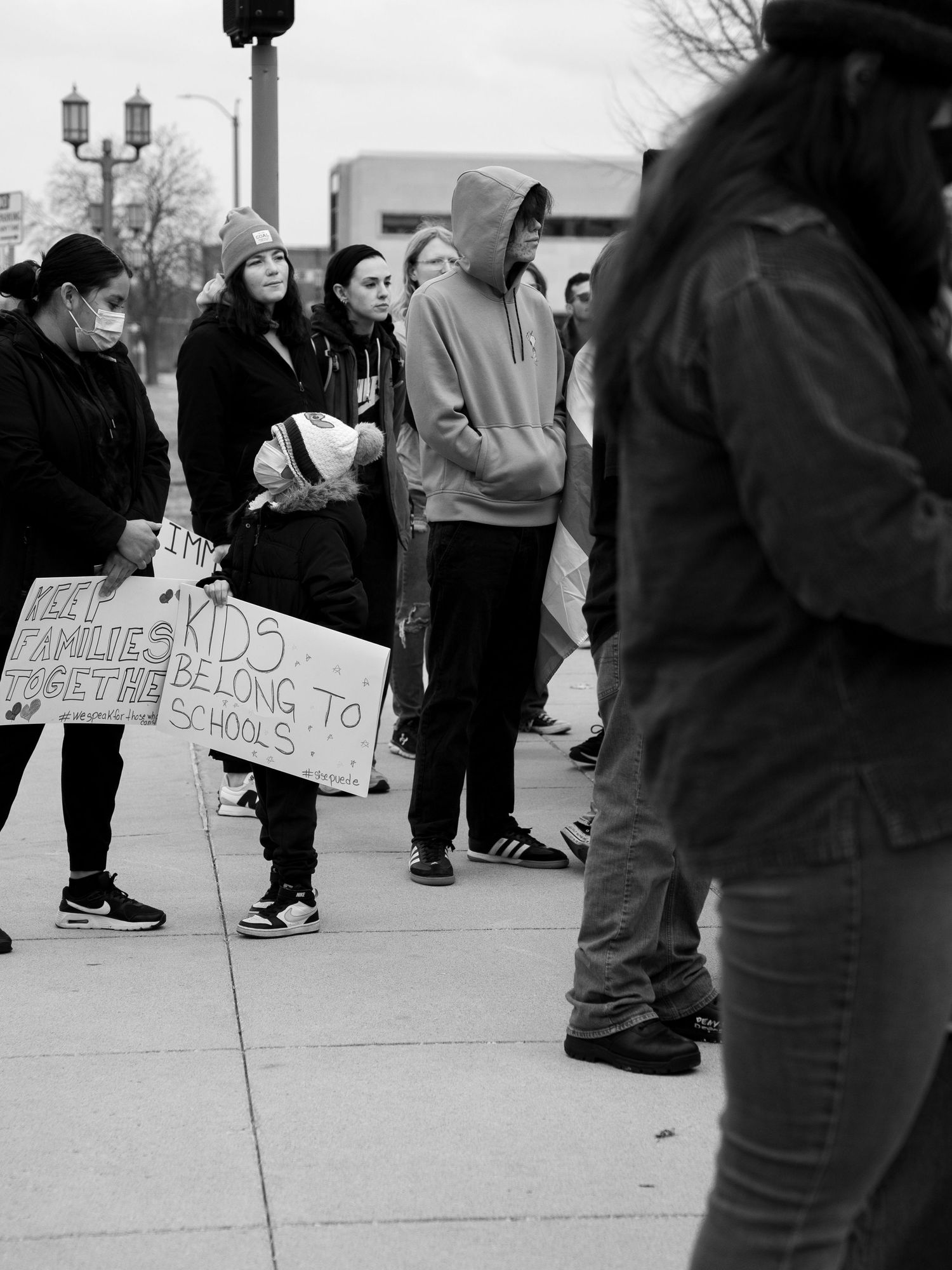 Black and white image of protesters gathered on a sidewalk with protest signs.