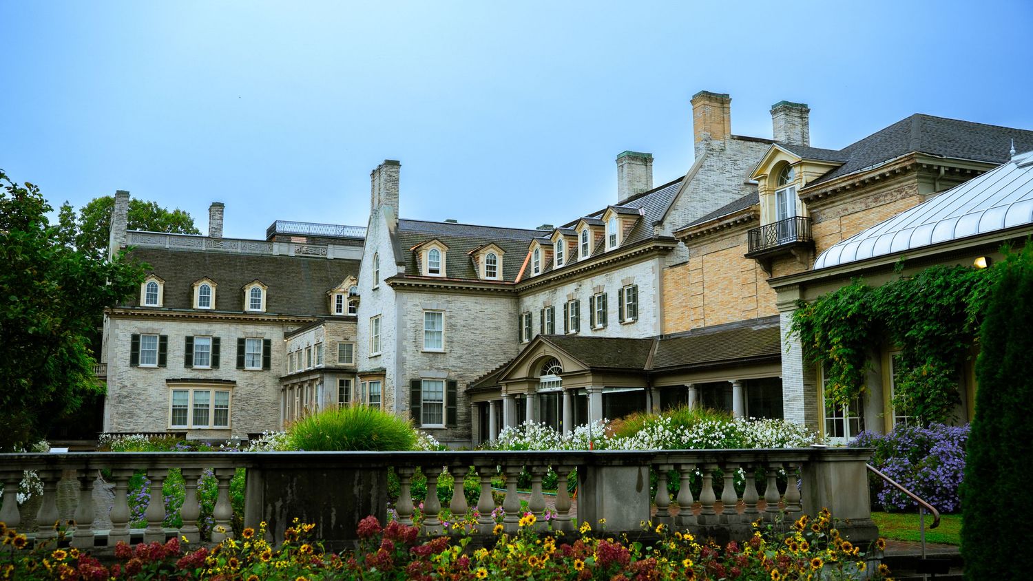Elegant stone mansion with dormers and landscaped grounds viewed in a panoramic format.