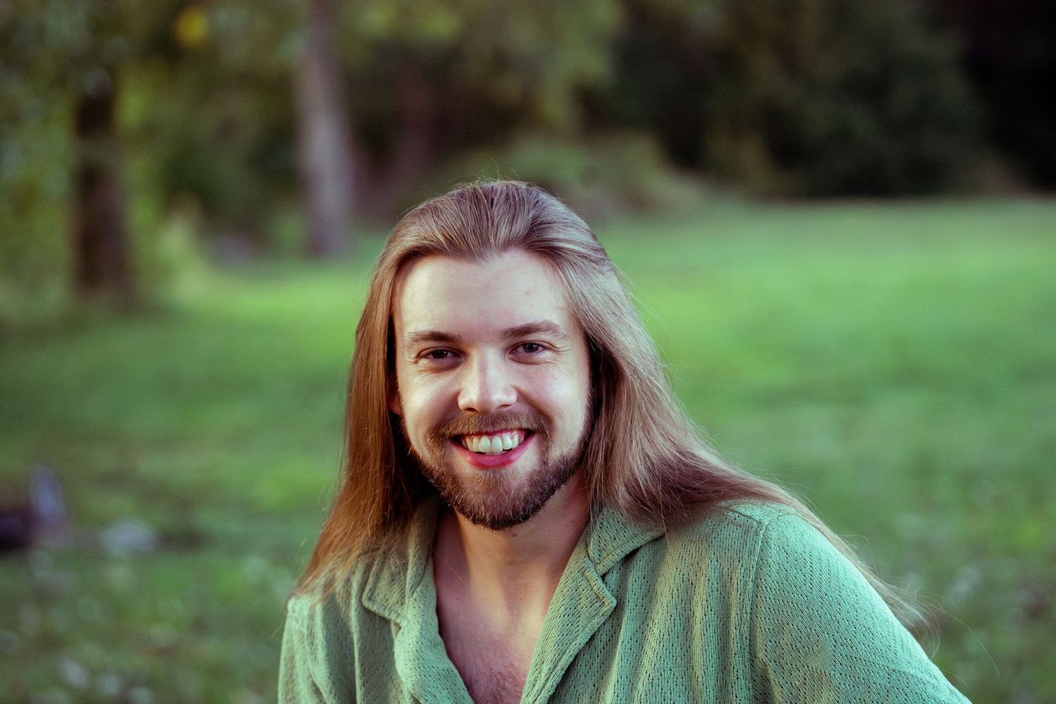 Person with long hair sitting in a grassy field during golden hour.