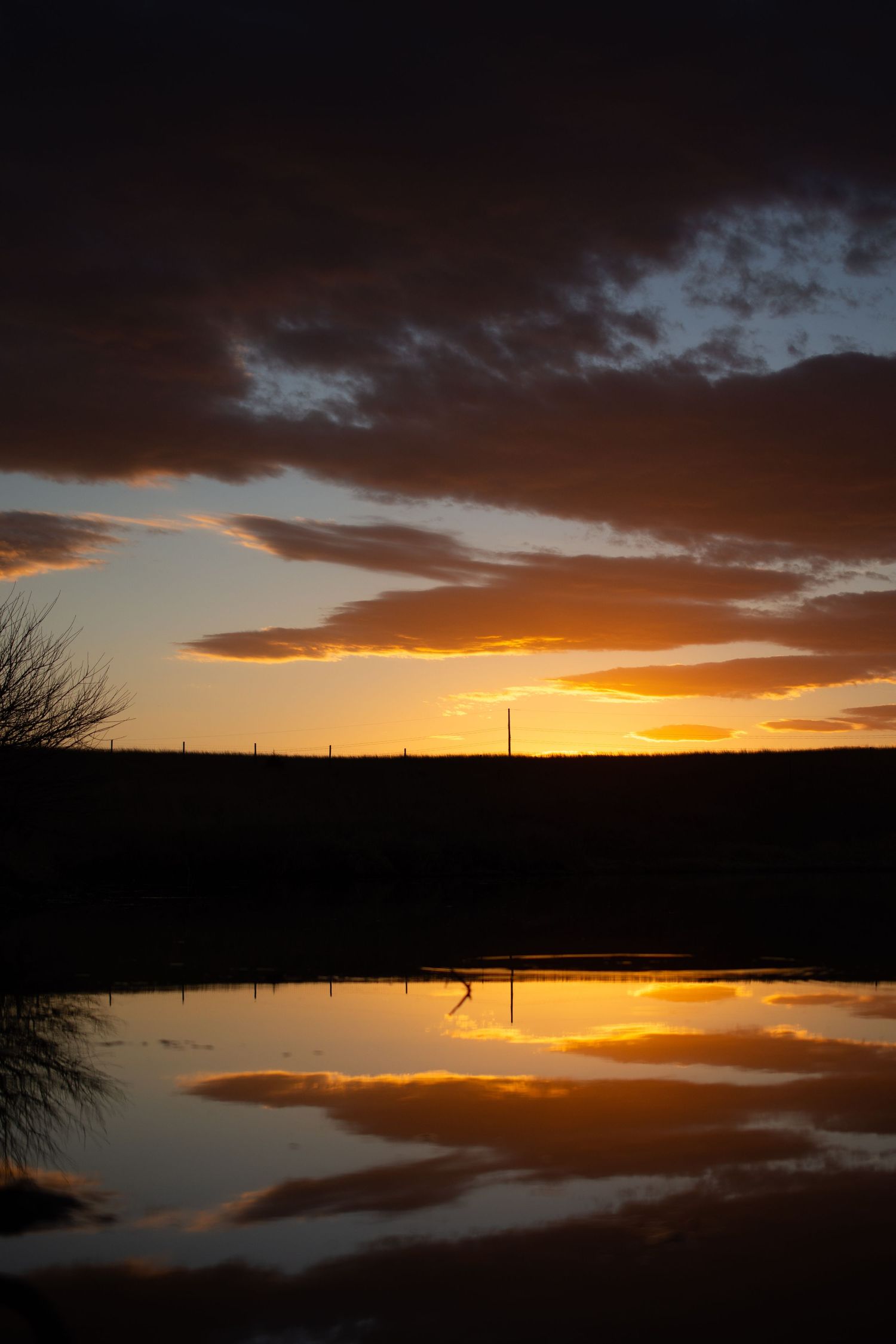 Dramatic orange sunset reflected in still water with silhouetted landscape.