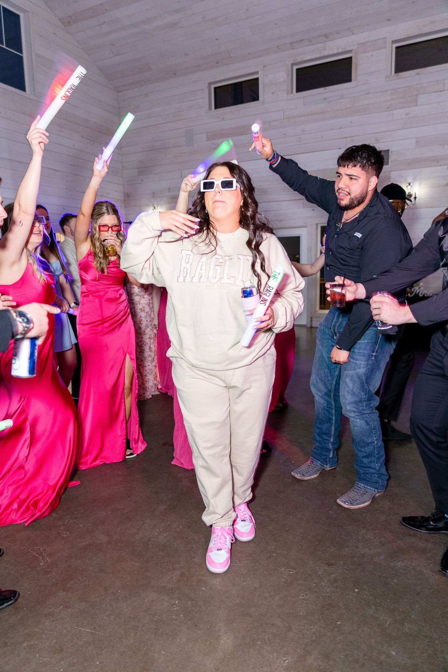Wedding reception dance party with guests holding colorful light sticks and dancing.