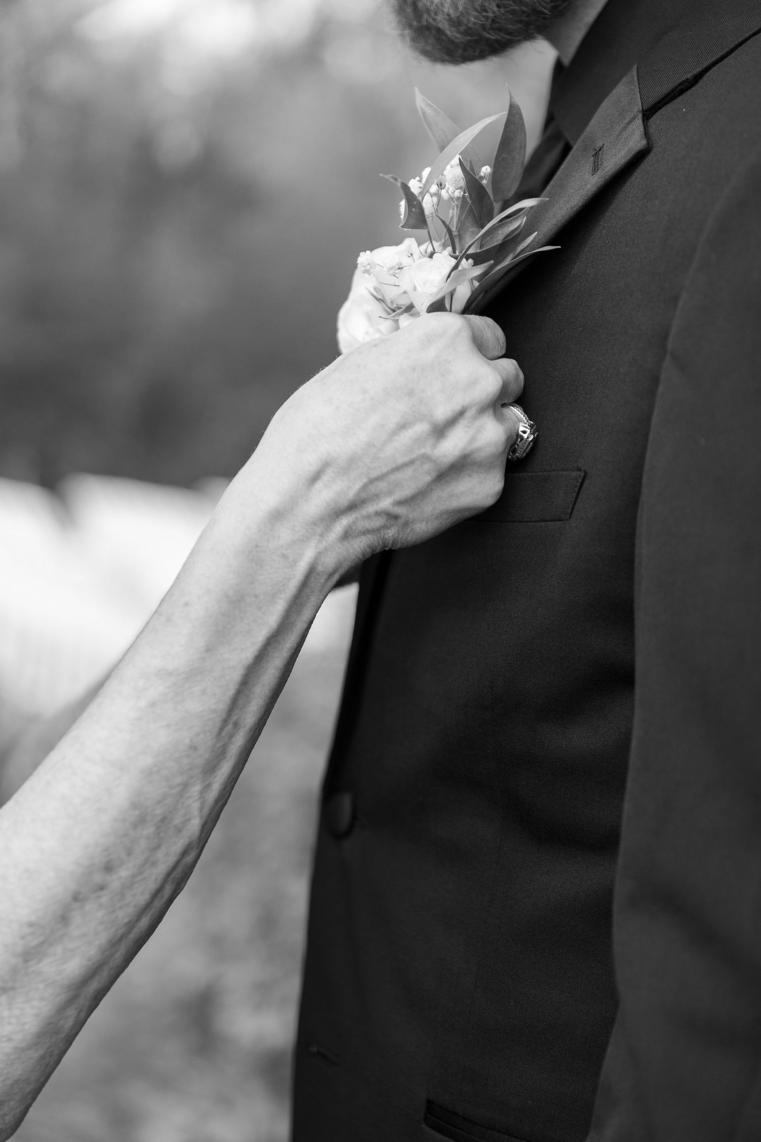 Close-up details of boutonnieres being pinned on dark suits at a formal event.