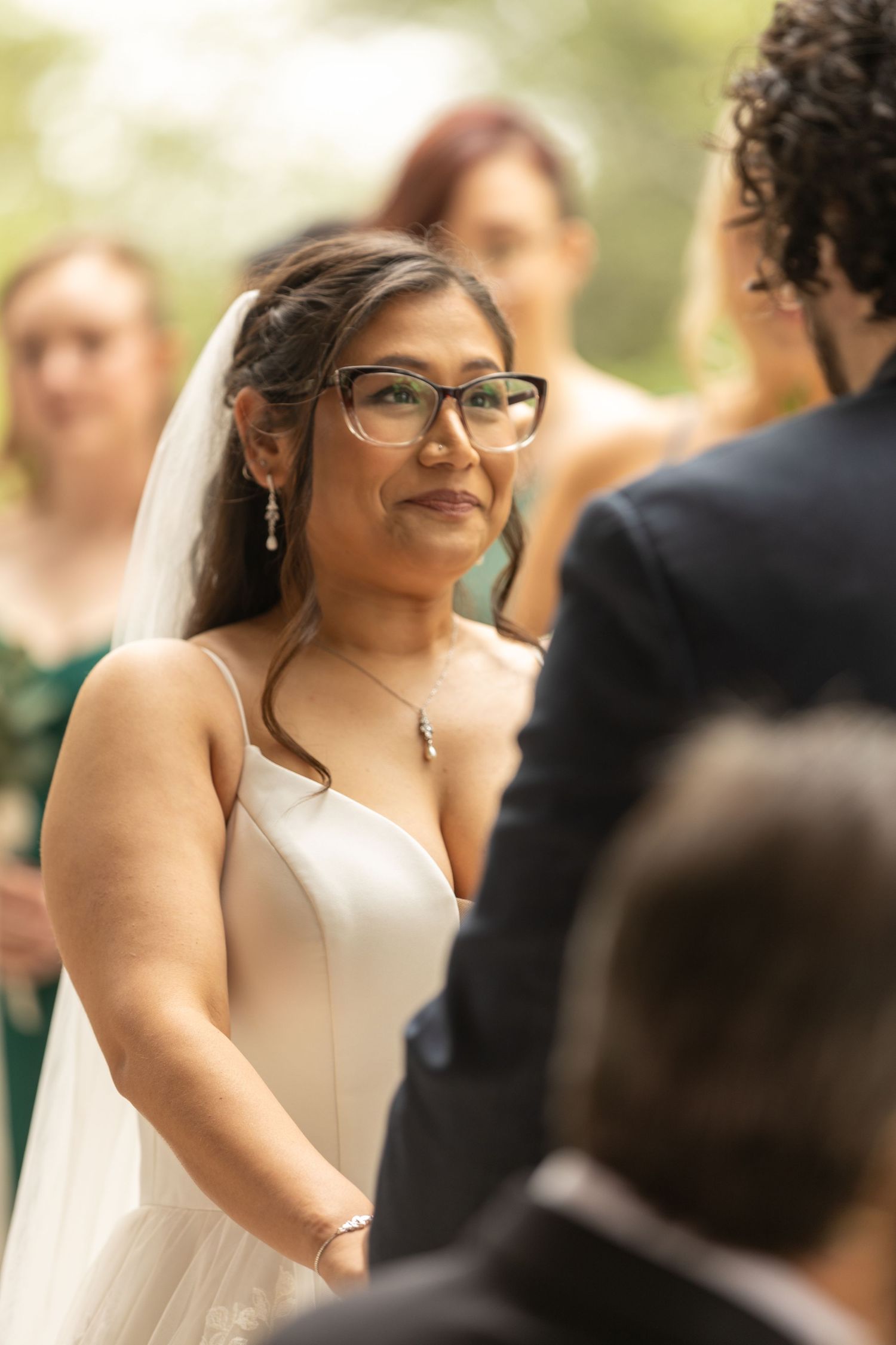 Close-up shots of a bride in glasses and white dress smiling during her wedding ceremony.