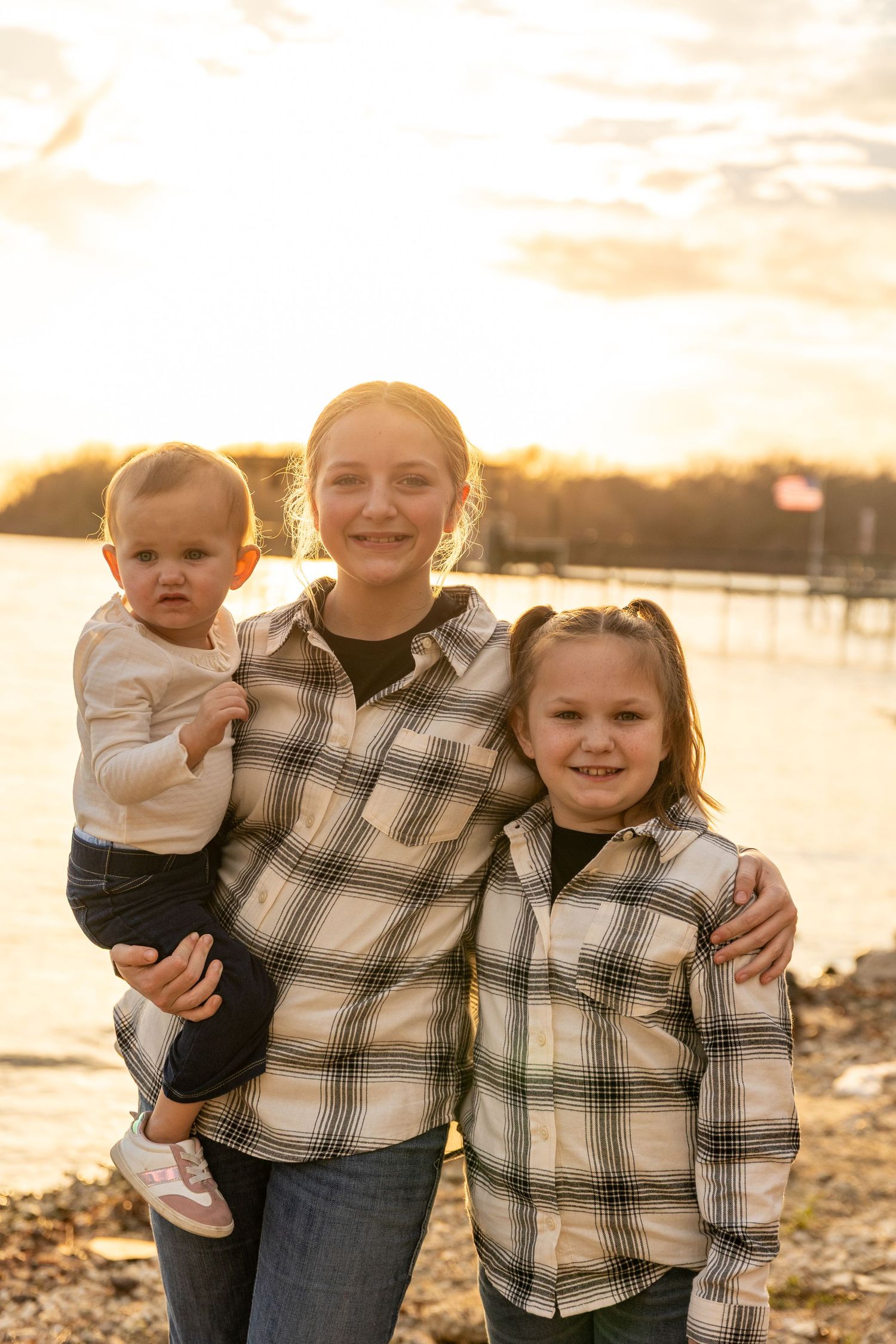 Family portrait at sunset by the water wearing plaid and casual clothing.