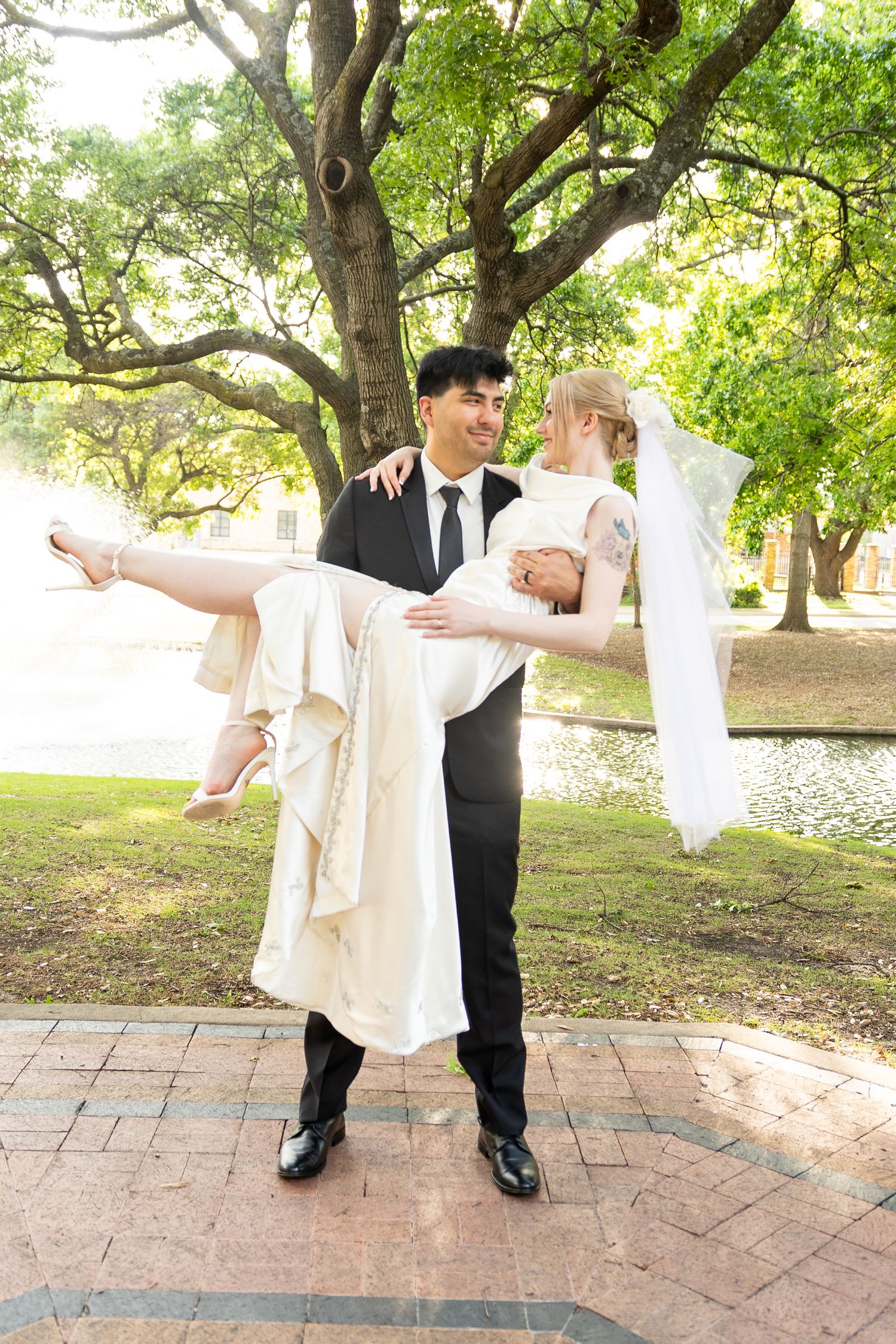 A couple dances playfully on a brick patio surrounded by lush green trees.