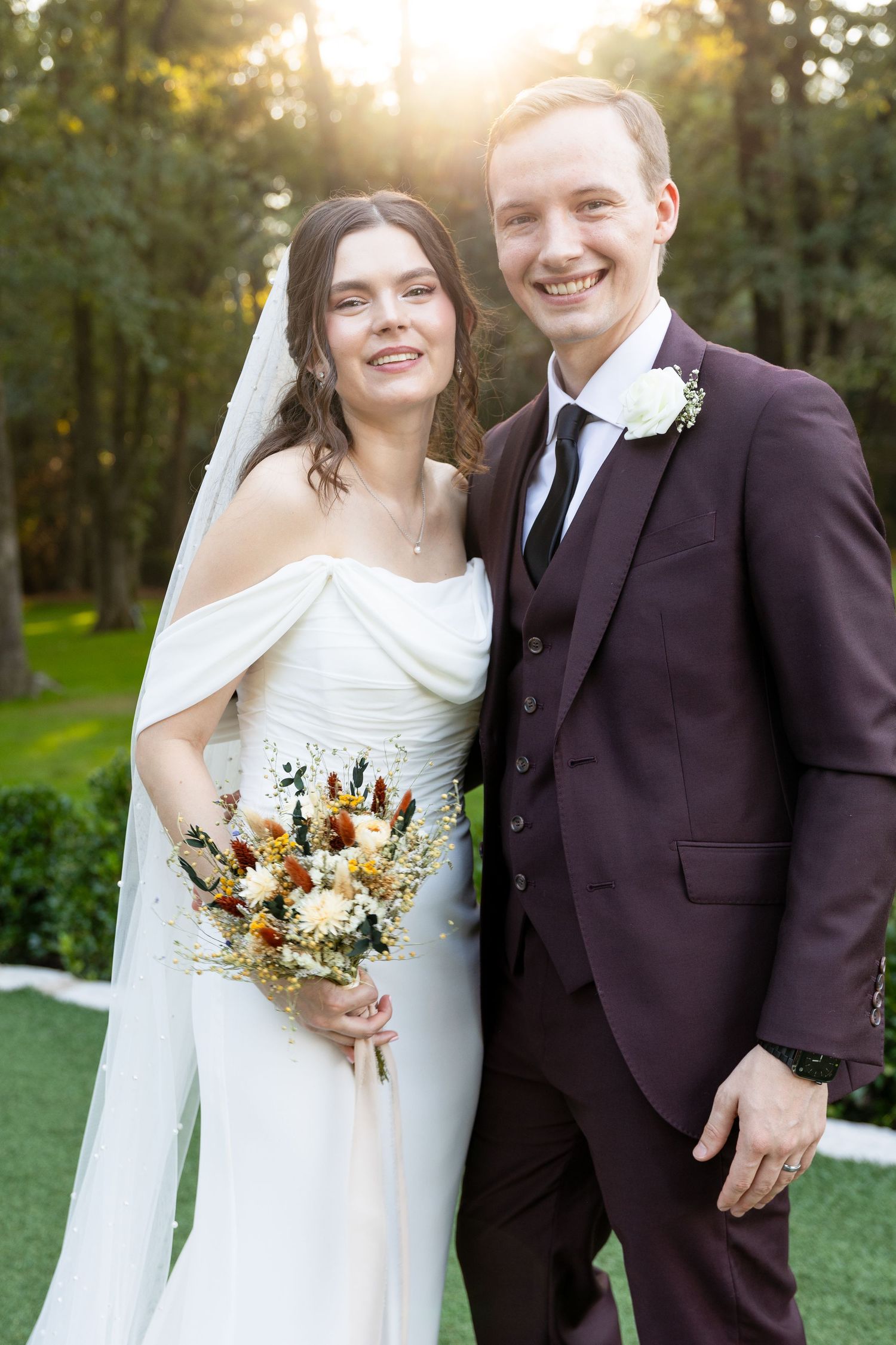 Wedding couple poses with autumn-themed bouquet in outdoor garden setting.