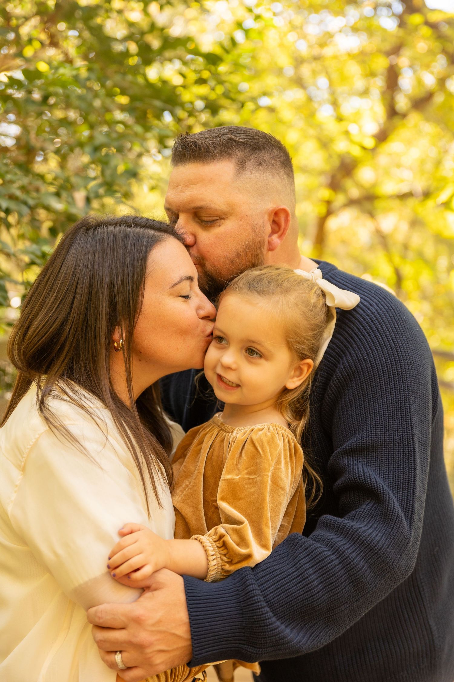 Family shares tender moments in golden autumn sunlight during outdoor photo session.