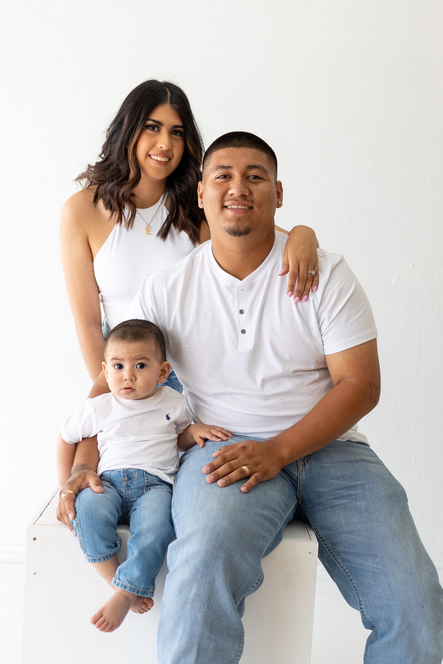 Family wearing coordinated white tops and jeans poses against white backdrop.