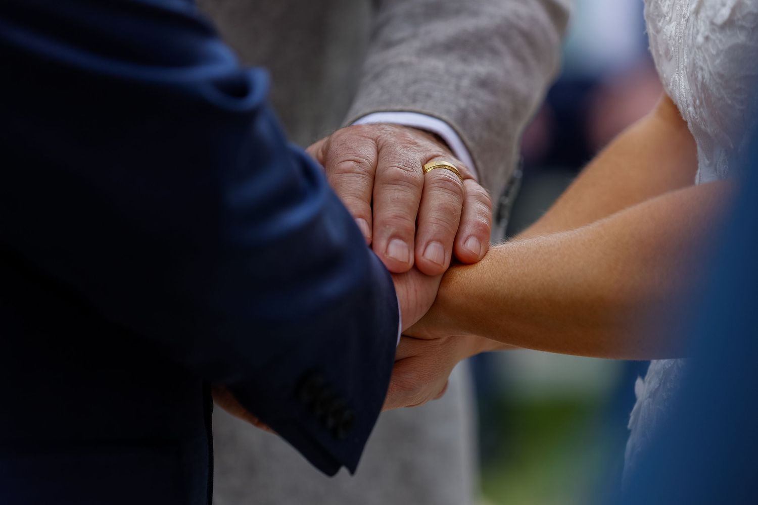 Close-up detail of hands and rings during outdoor wedding ceremony.